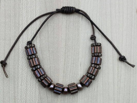 A casual leather slider bracelet of baroque freshwater in plum and antique copper plated ceramic steampunk styled beads.