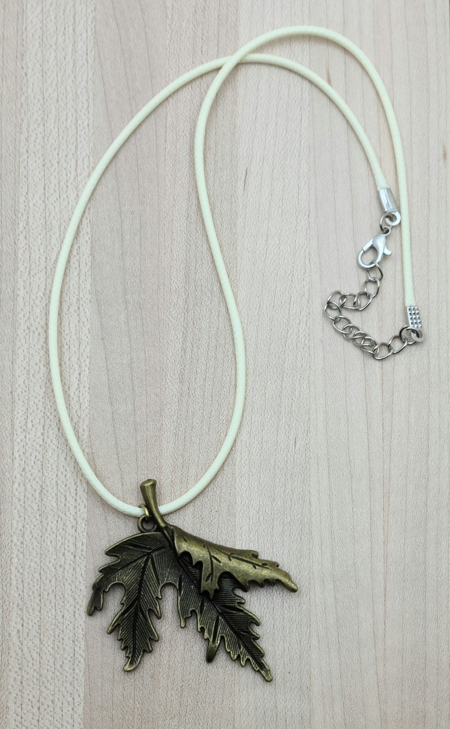 A brass folded leaf pendant on a cream colored cordis perfect for Fall!