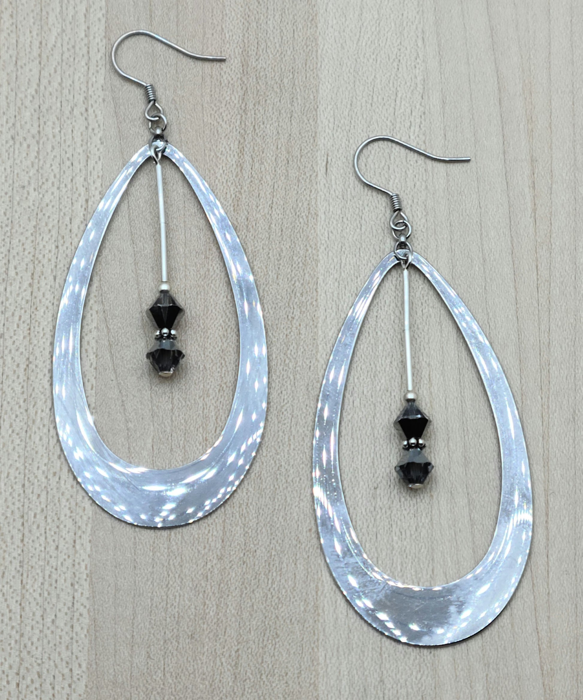 Large stainless steel hoop teardrop earrings with crystals hanging down the center.