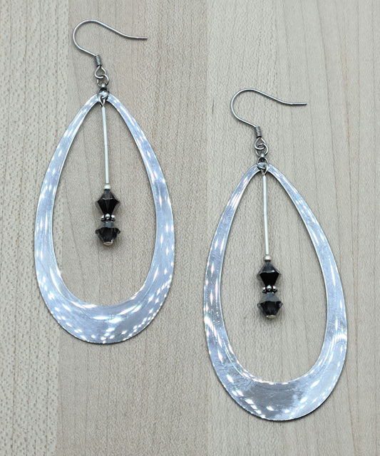 Large stainless steel hoop teardrop earrings with crystals hanging down the center.