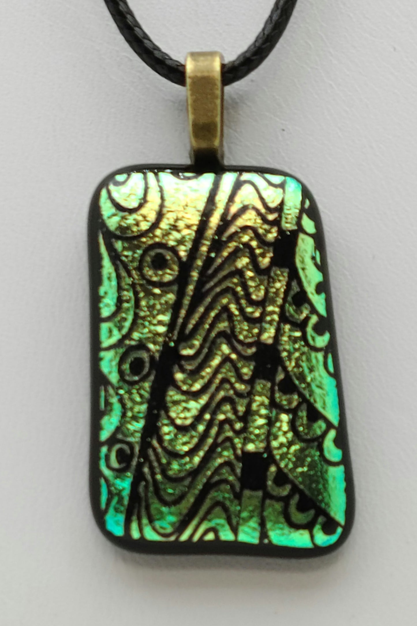 bits of geometrics are etched into this green dichroic fused glass pendant.