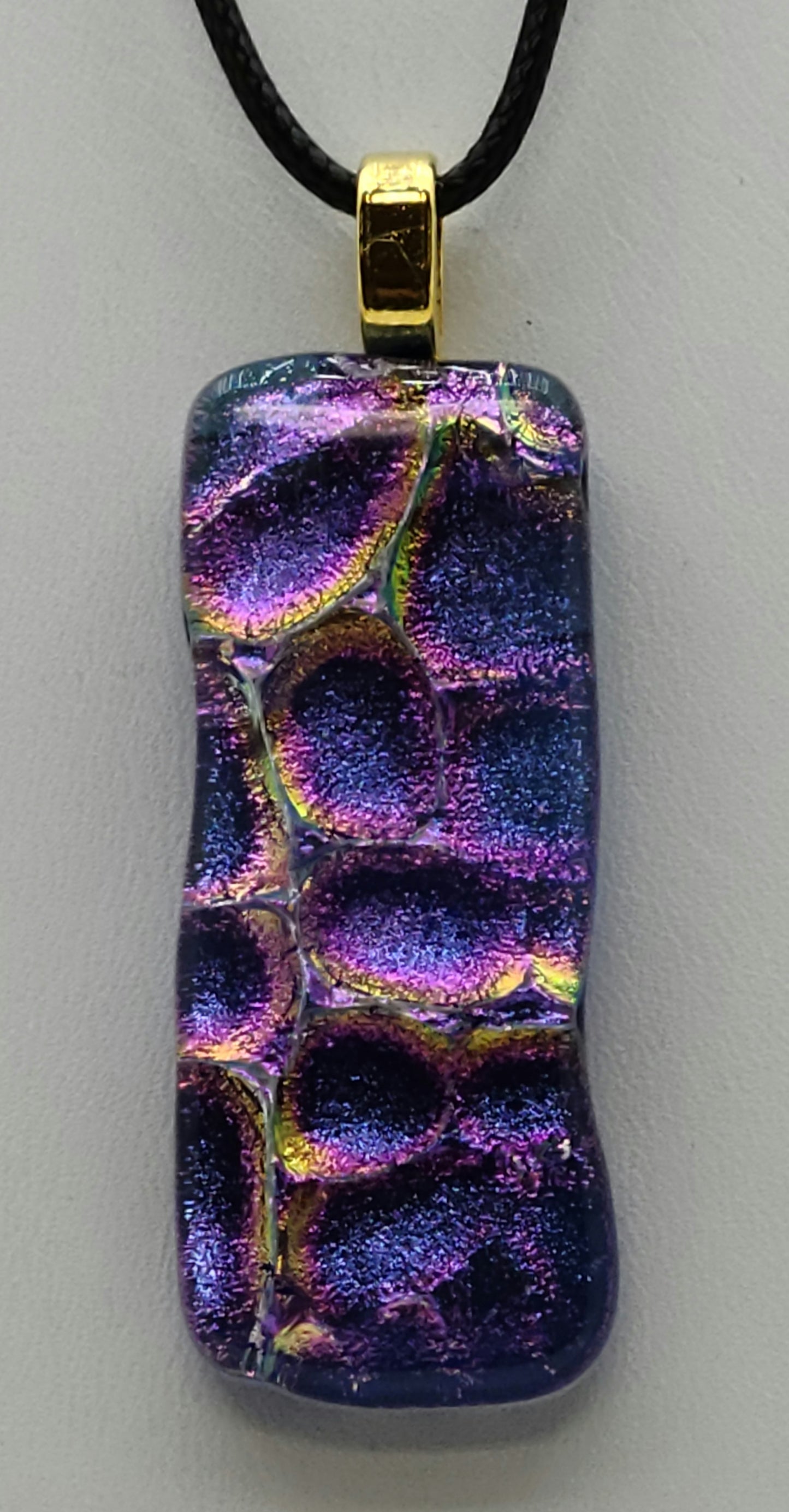 This long, slender dichroic fused glass pendant is bluish purple with hints of gold & fuchsia.
