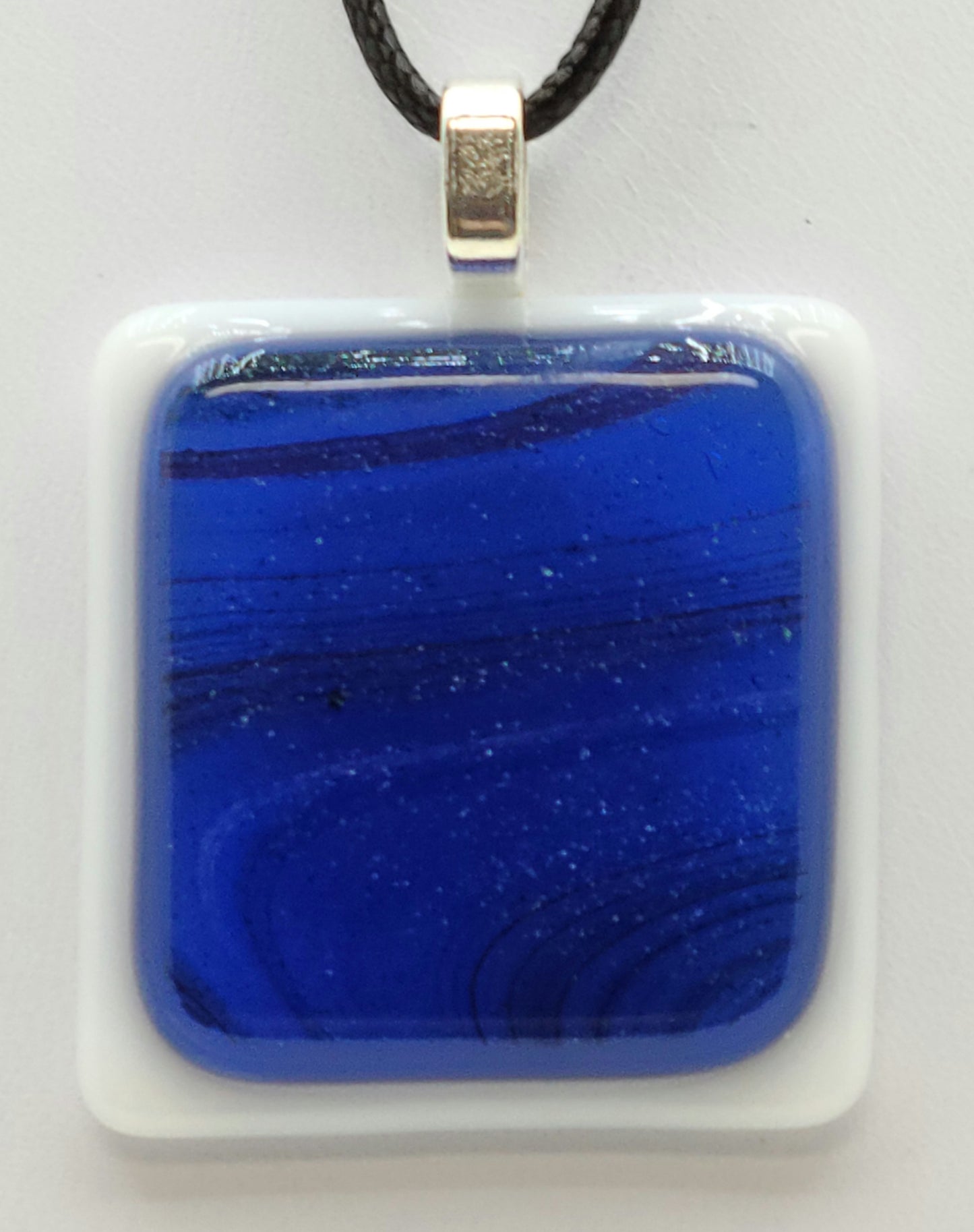glittery swirls of blue against a white background in this fused glass pendant