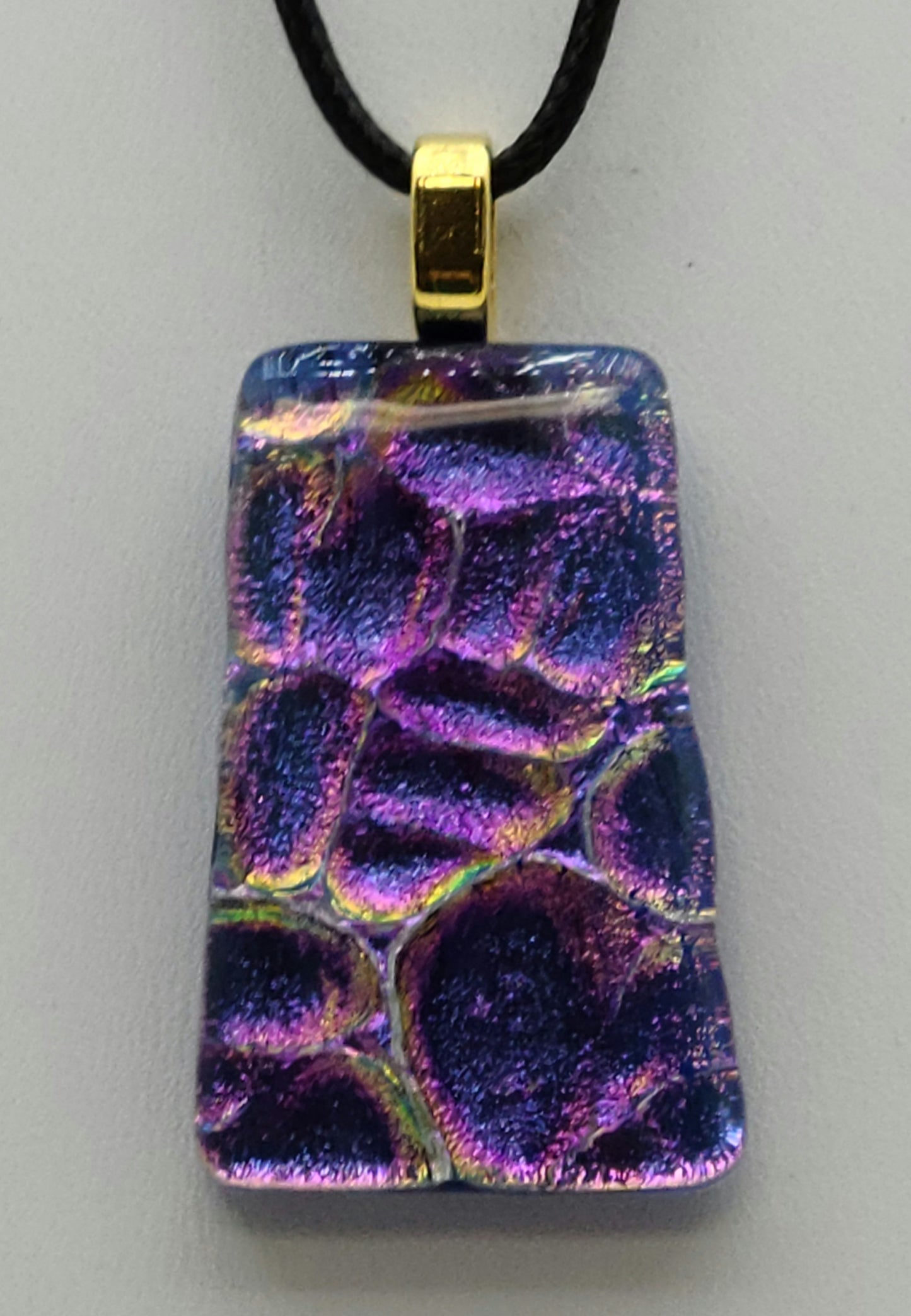This trapezoid dichroic fused glass pendant is bluish purple with hints of gold & fuchsia.