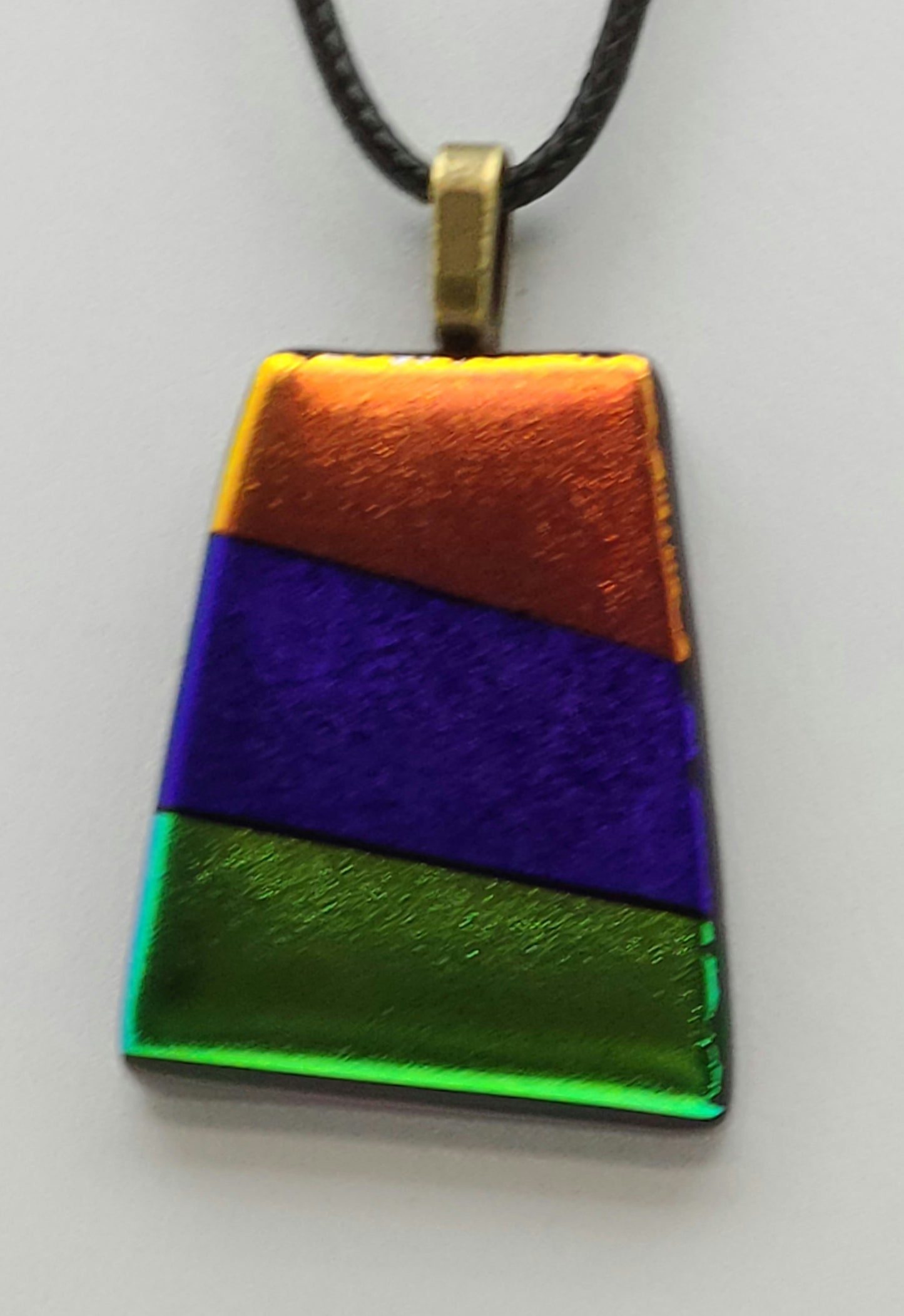 This dichroic fused glass pendant features bold stripes of gold, purple, & green.