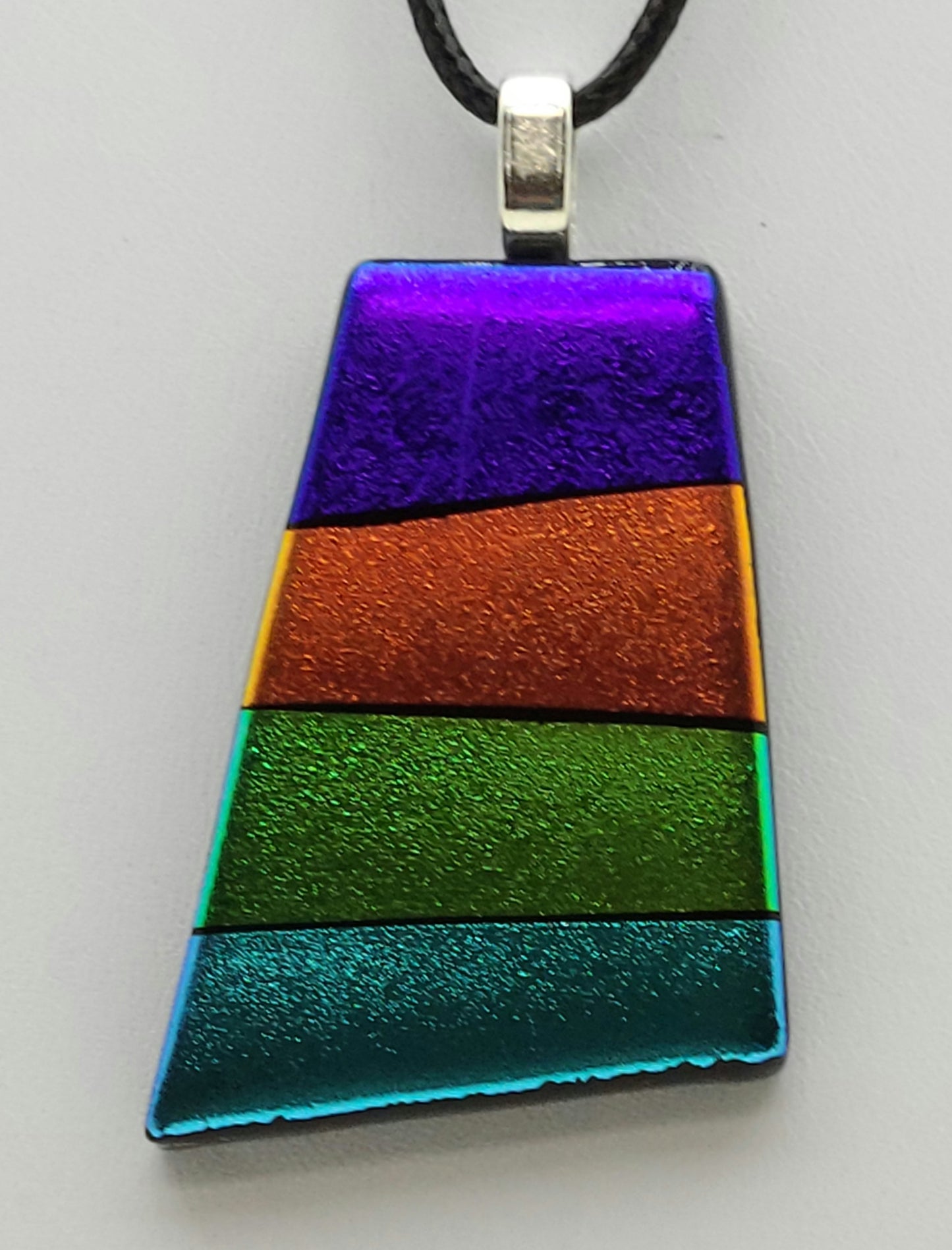 This dichroic fused glass pendant features rows of purple, gold, green, & turquoise
