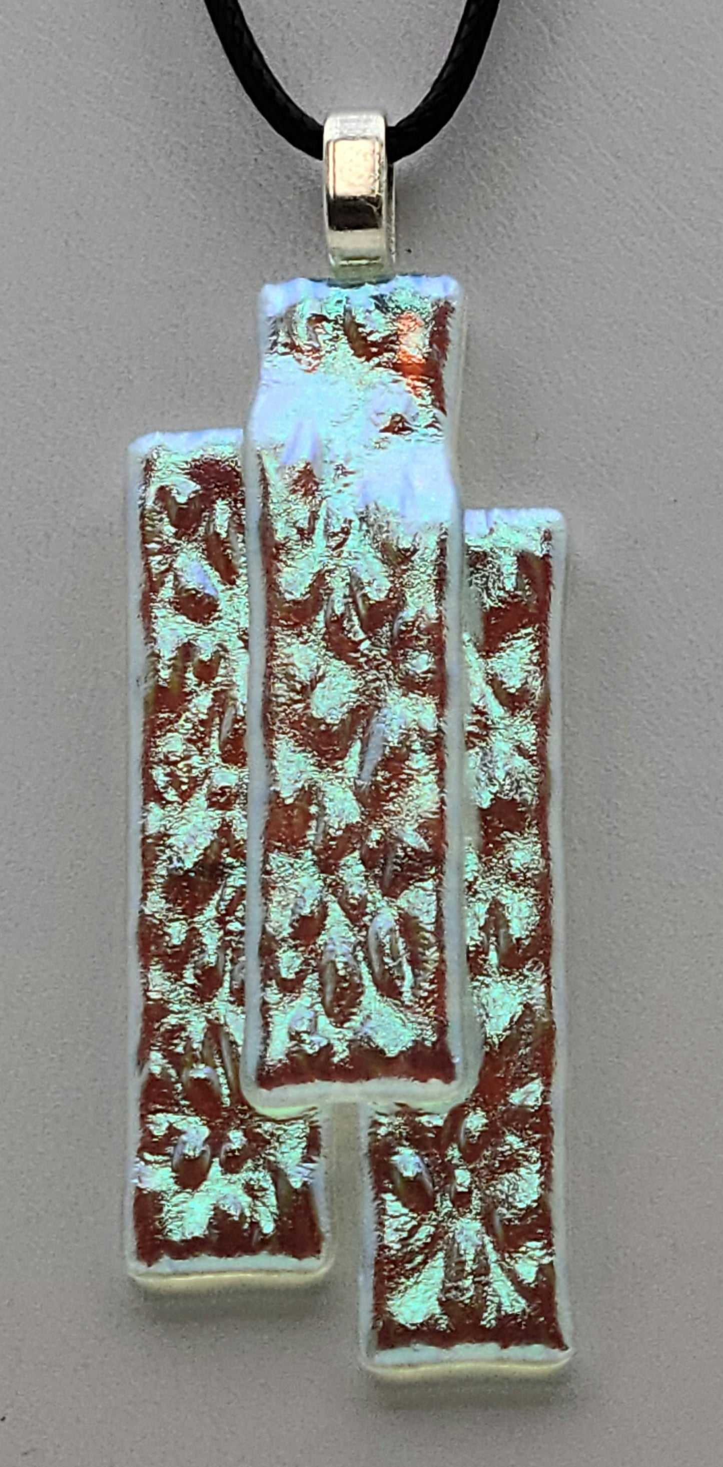 This stacked dichroic fused glass pendant will take on the hue of the underlying clothing!