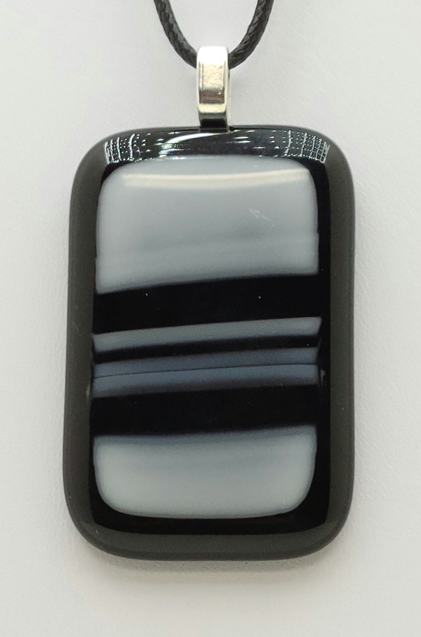 bold black strokes across white on an black background define this fused glass pendant.