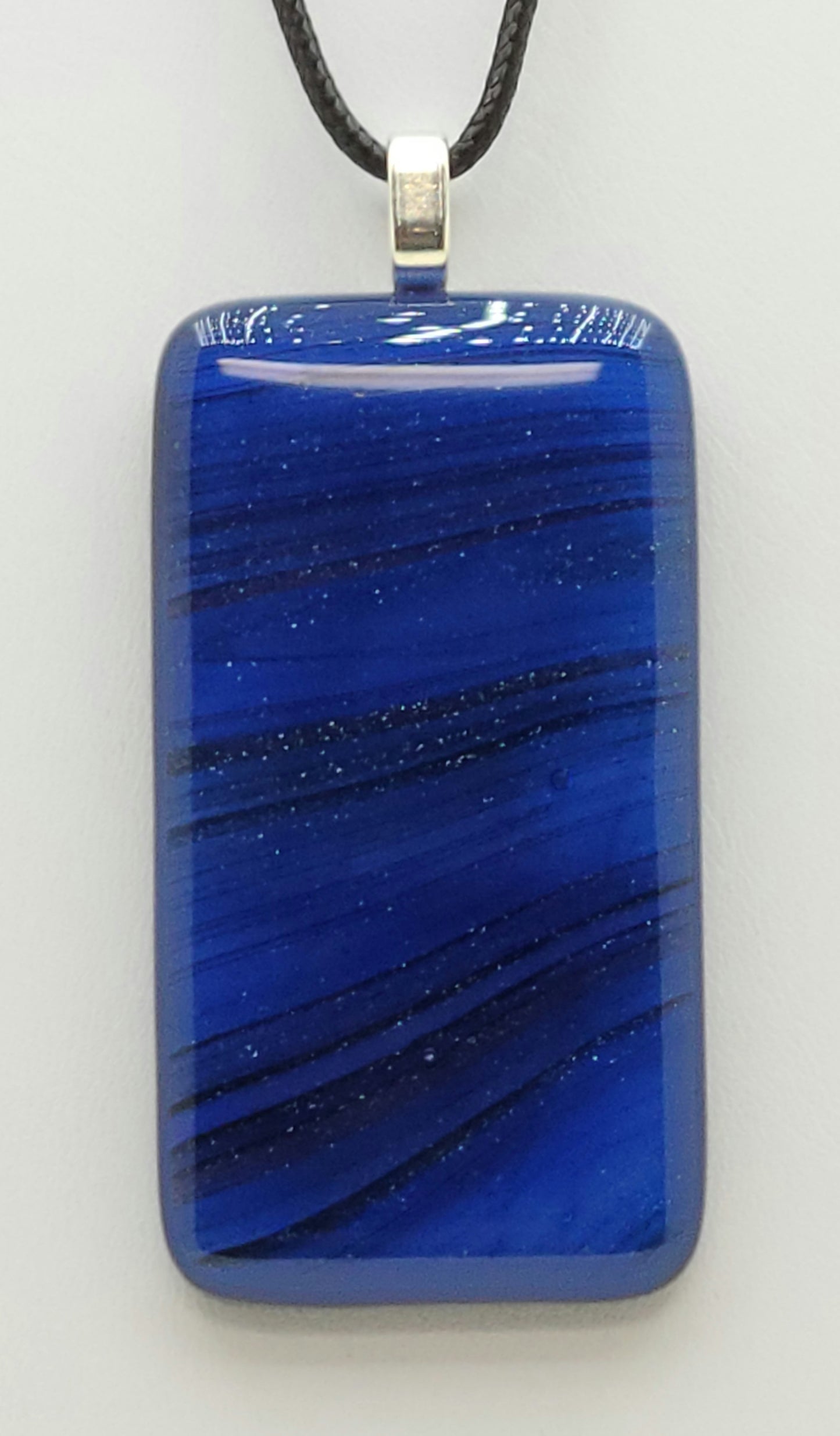 waves of sparkling blue stream across the glittery fused glass pendant.