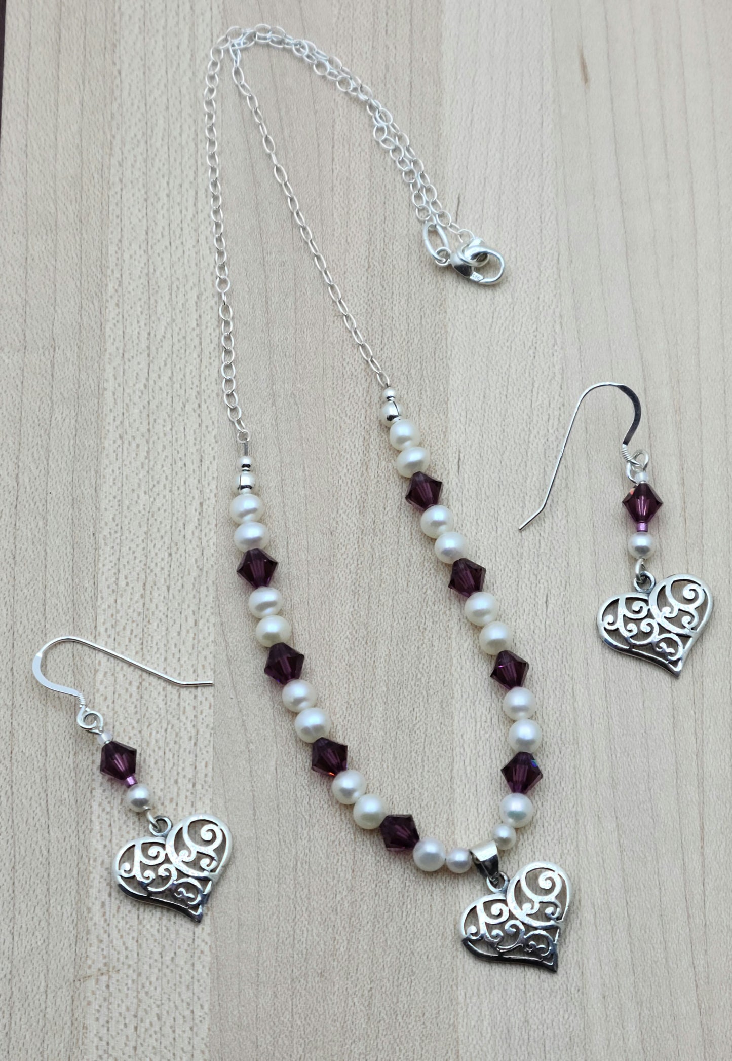 This sophisticated & sweet set features luminous white freshwater pearls & vibrant amethyst crystals, accented by a delicate filigree sterling silver heart pendant with matching earrings