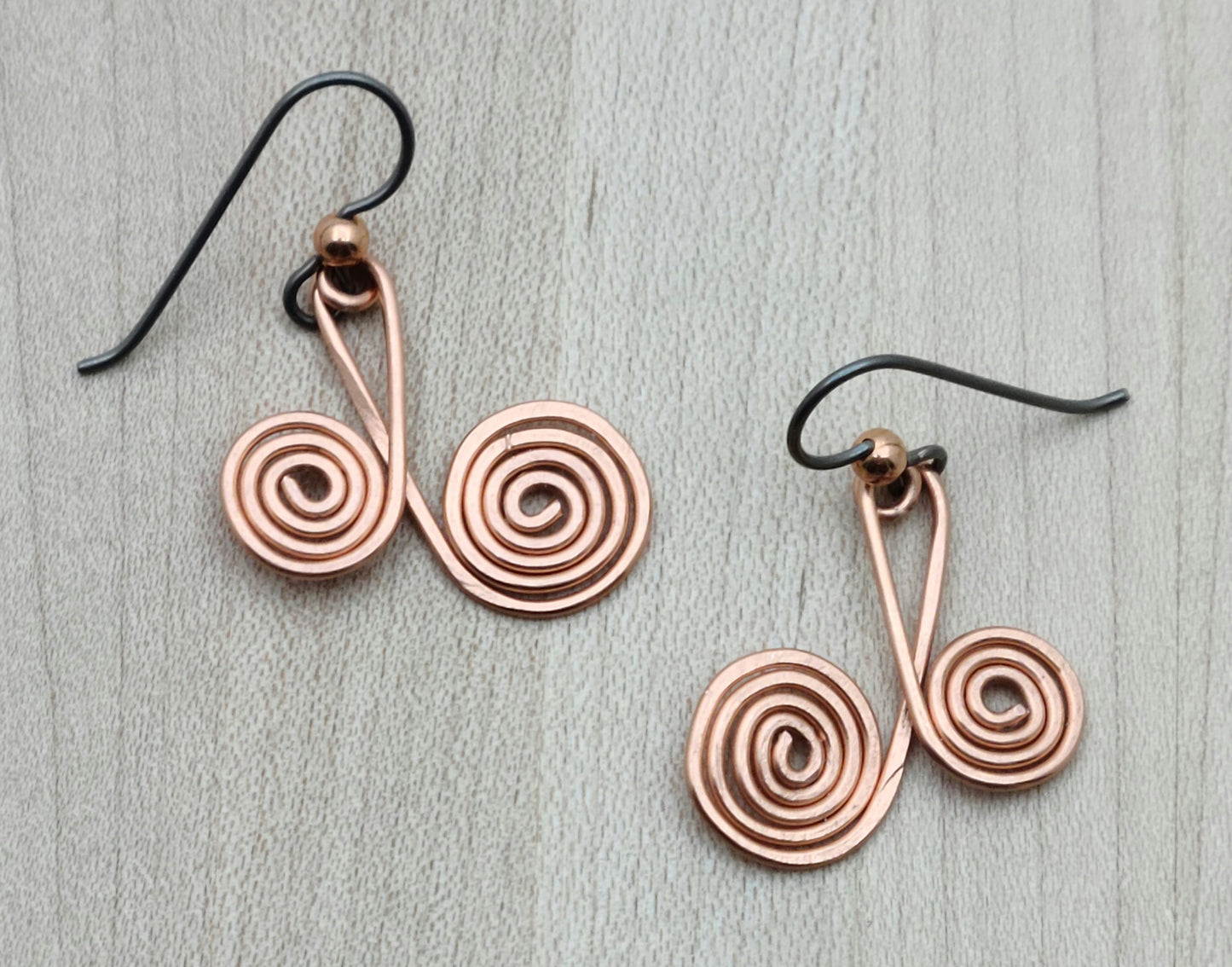 Add a touch of playful charm with these Copper Spiral Earrings. Each earring showcases two sizes of hammered copper spirals, creating a lively, eye-catching look. They hang comfortably on hypoallergenic niobium French hooks, making them gentle on sensitive ears. Perfect for brightening up any outfit with a fun, artistic vibe.