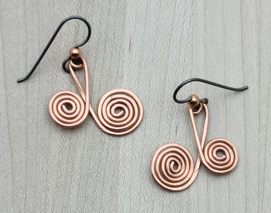 Add a touch of playful charm with these Copper Spiral Earrings. Each earring showcases two sizes of hammered copper spirals, creating a lively, eye-catching look. They hang comfortably on hypoallergenic niobium French hooks, making them gentle on sensitive ears. Perfect for brightening up any outfit with a fun, artistic vibe.
