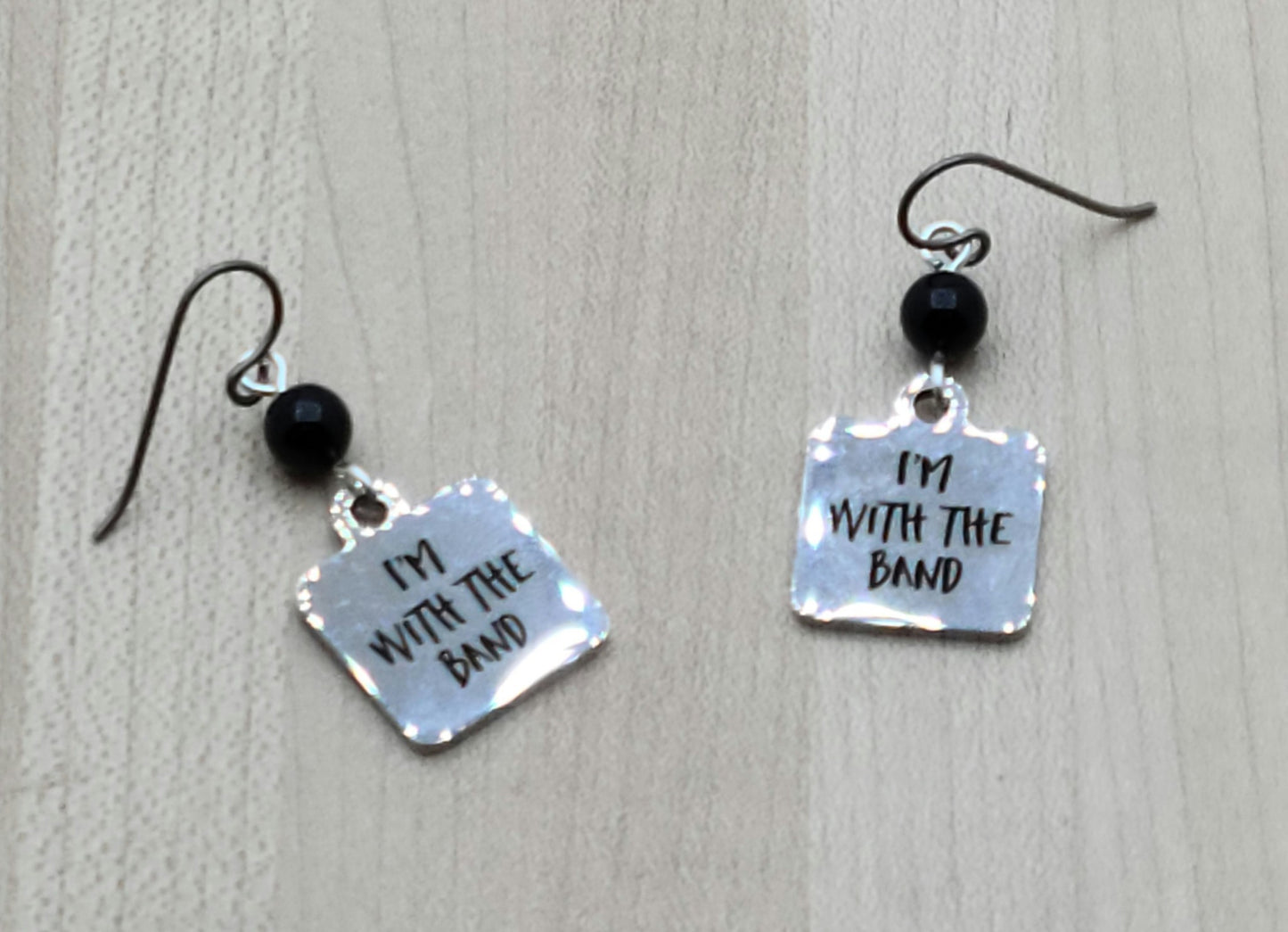 Proudly announce that you are indeed "with the band" by wearing these shiny stainless steel earrings suspended from black crystal pearls.