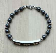 An antique silver bar sporting a tribal design is surrounded by pewter beads & grounding hematite.