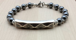 An antique silver bar sporting a tribal design is surrounded by pewter beads & grounding hematite.
