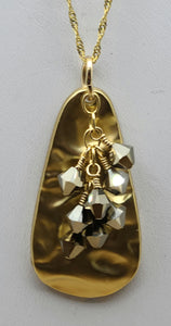 A large gold plated, hammered pewter teardrop is adorned with crystals* of metallic light gold hanging from a gold filled chain.