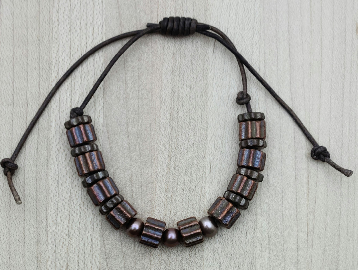 A casual leather slider bracelet of baroque freshwater in plum and antique copper plated ceramic steampunk styled beads.