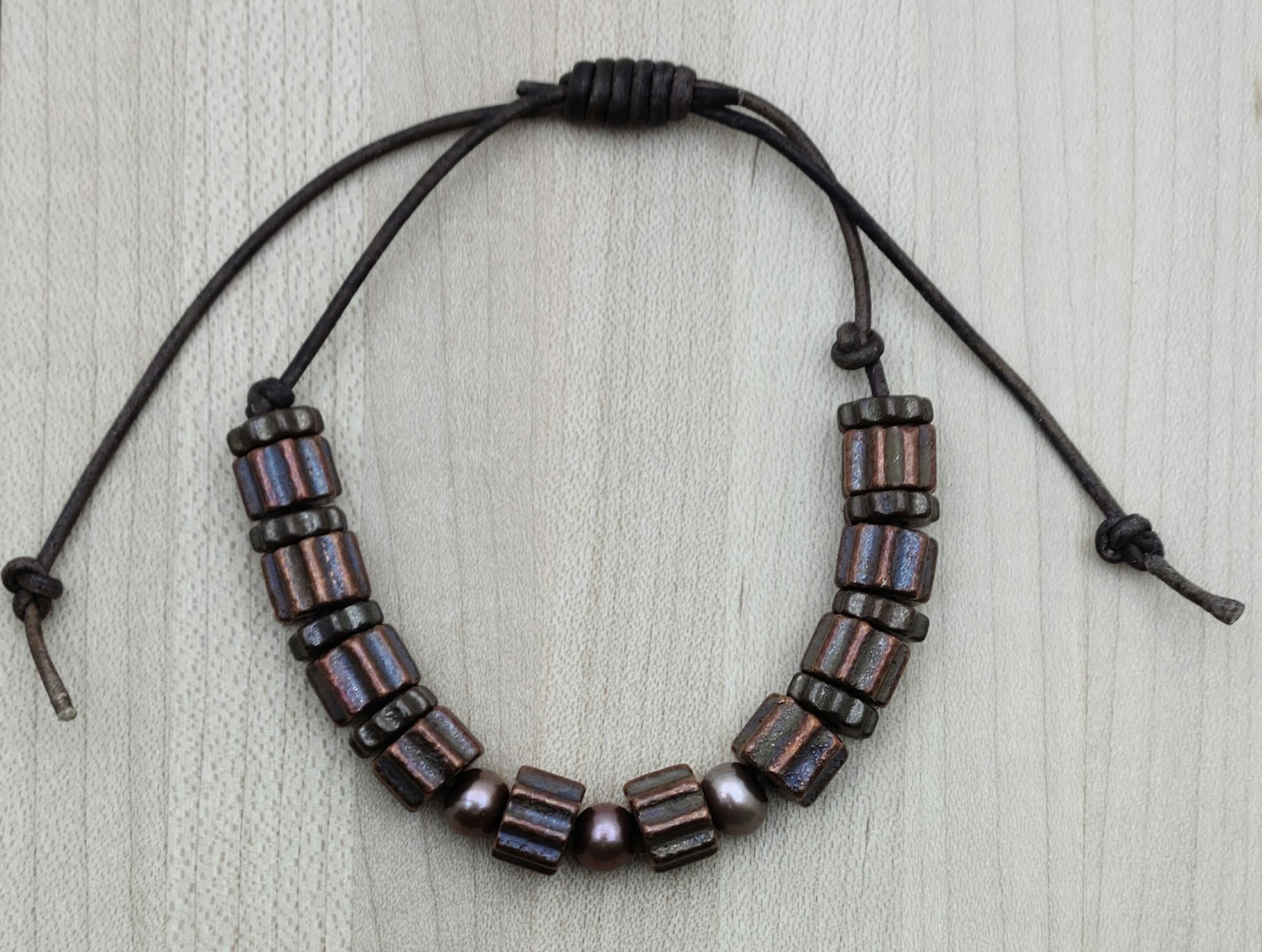 A casual leather slider bracelet of baroque freshwater in plum and antique copper plated ceramic steampunk styled beads.