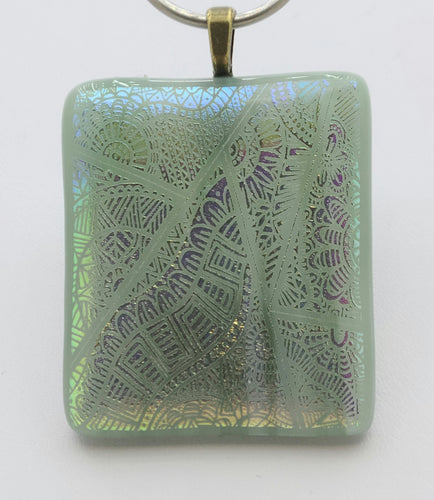 An etched dichroic cathedral window glass is fused to blue green glass & adds a stained glass effect to this fused glass pendant.