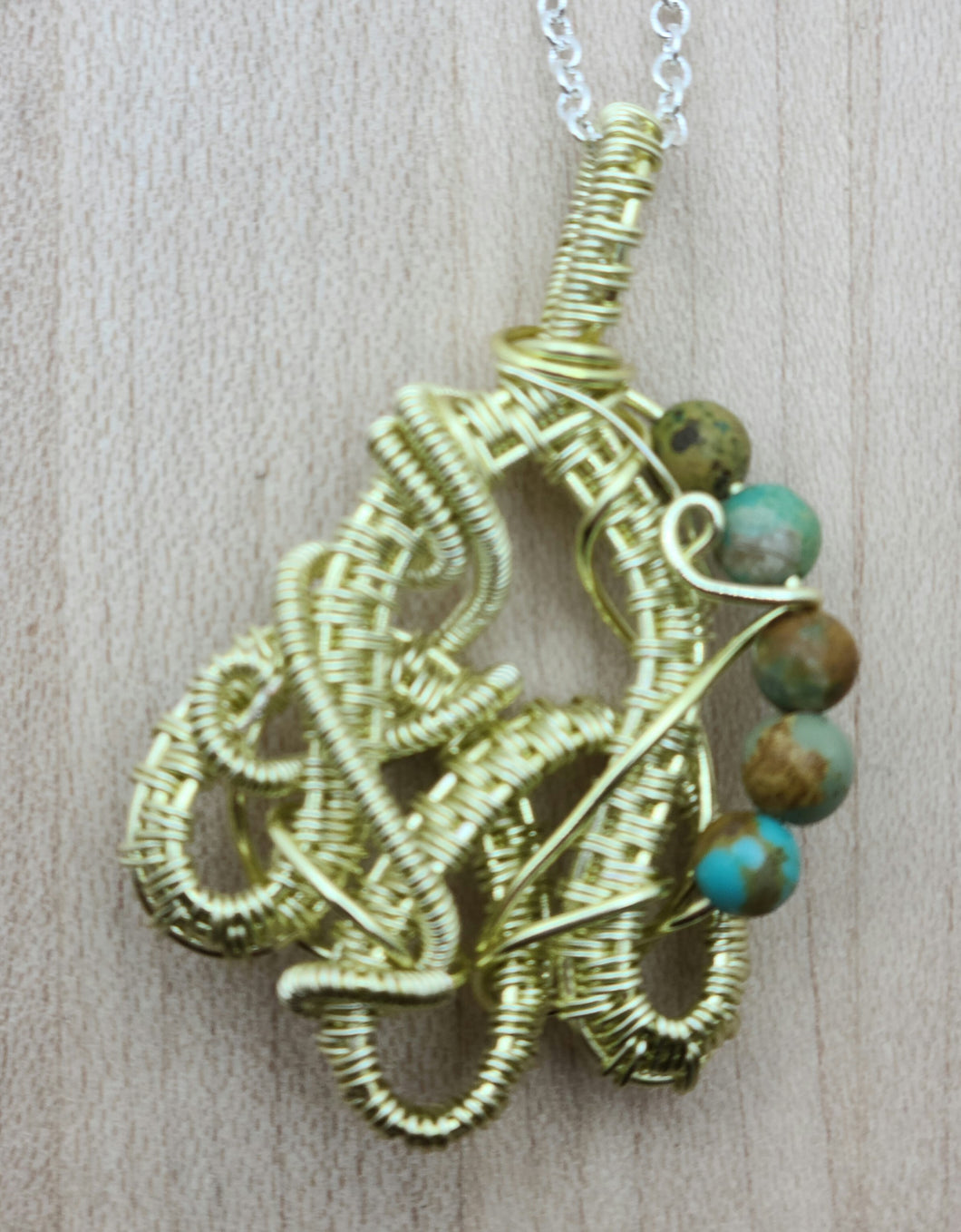 This interestingly shaped pendant of champagne colored tarnish resistant silver plated copper wire is accented with small turquoise beads.