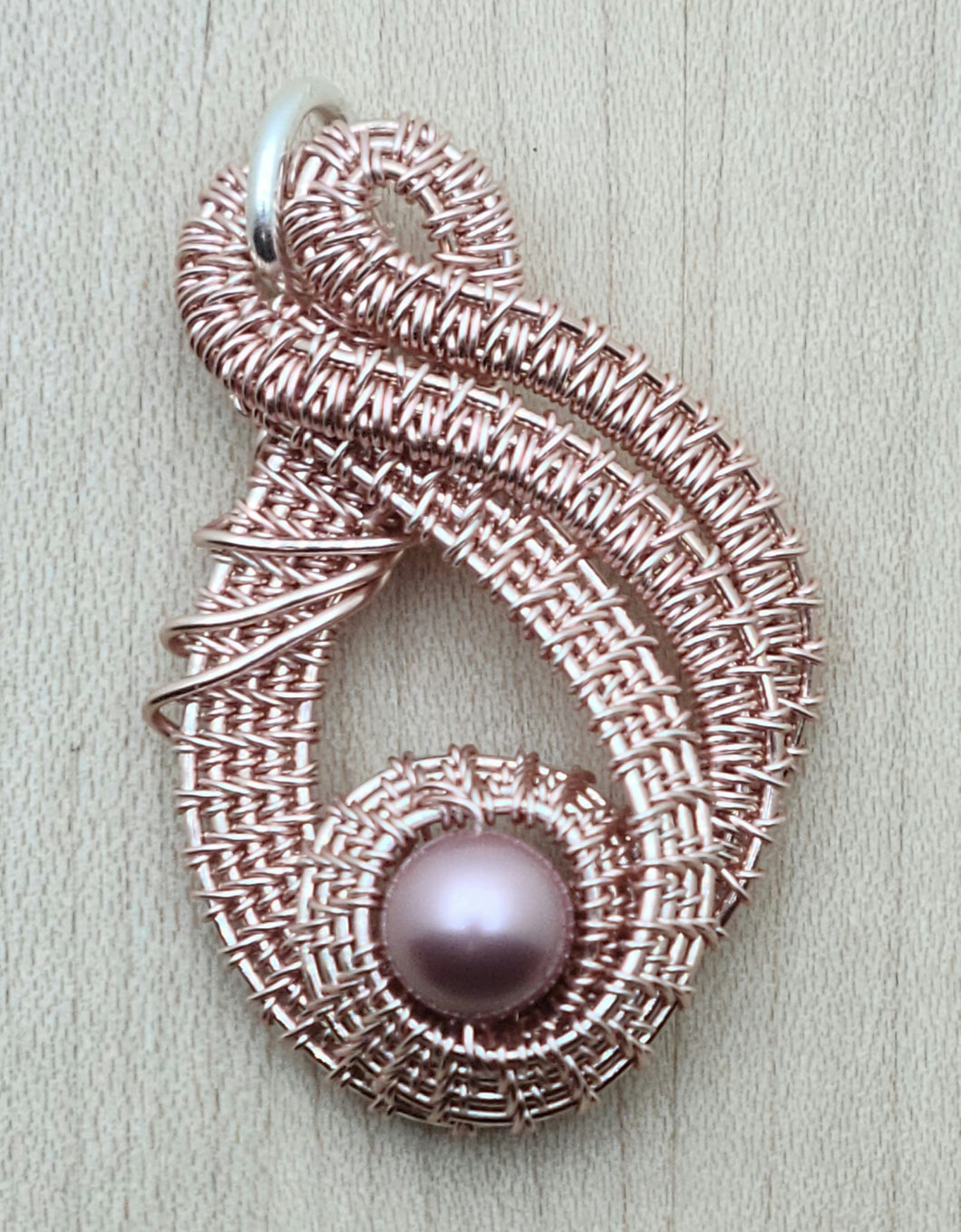 Expertly crafted with tarnish-resistant silver plating, this Woven Wire Rose Gold Pendant is a stunning accessory. The intricate woven wire design is accented with a crystal pearl in a soft powdered rose hue, adding elegance and sophistication to any outfit. Make a statement with this unique and beautiful pendant.