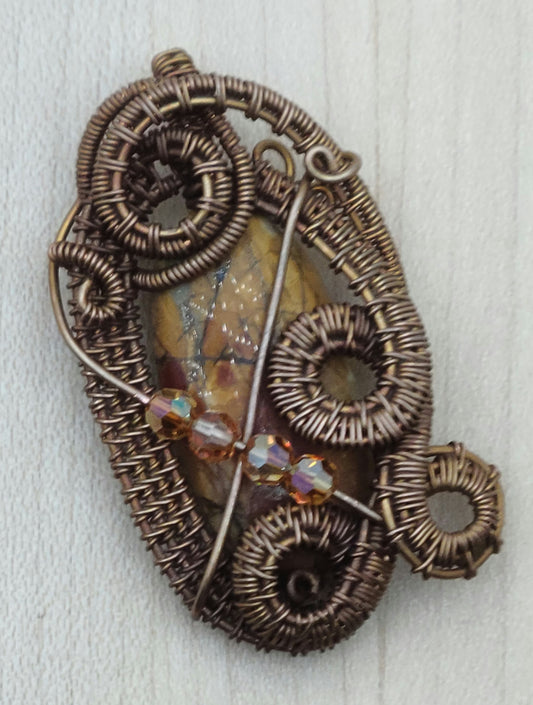 A Red Creek jasper stone is surround by a fancily woven frame of antiqued copper and adorned with crystals.