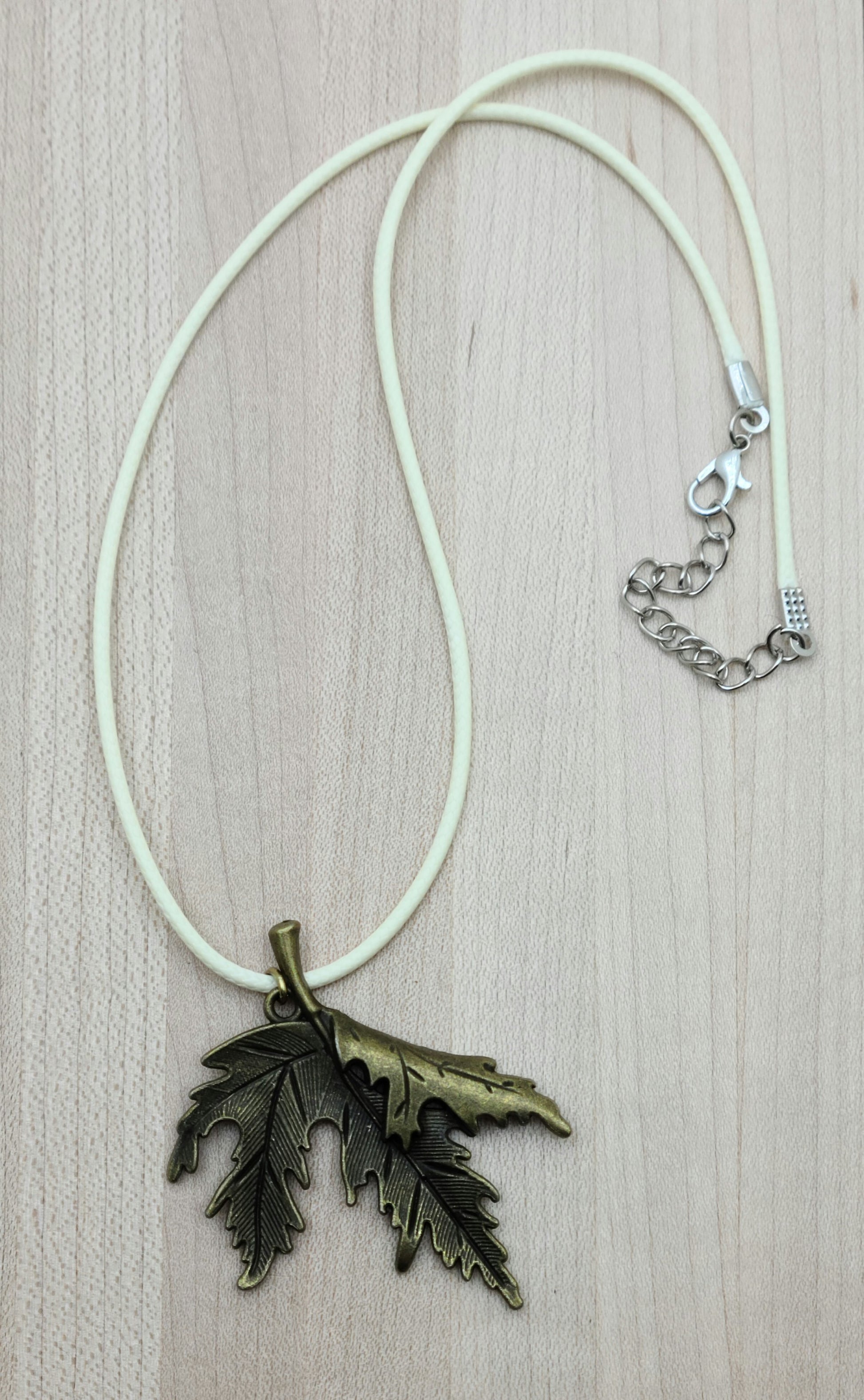 A brass folded leaf pendant on  a cream colored cordis perfect for Fall!