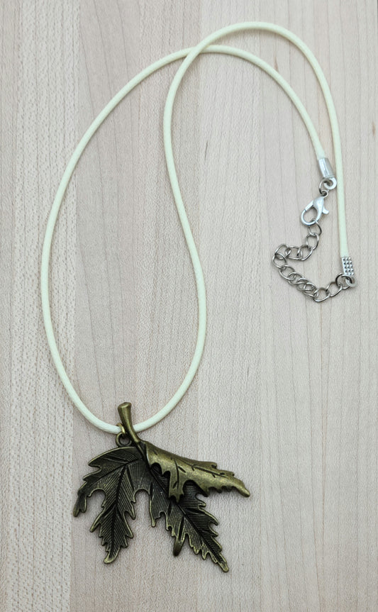A brass folded leaf pendant on  a cream colored cordis perfect for Fall!