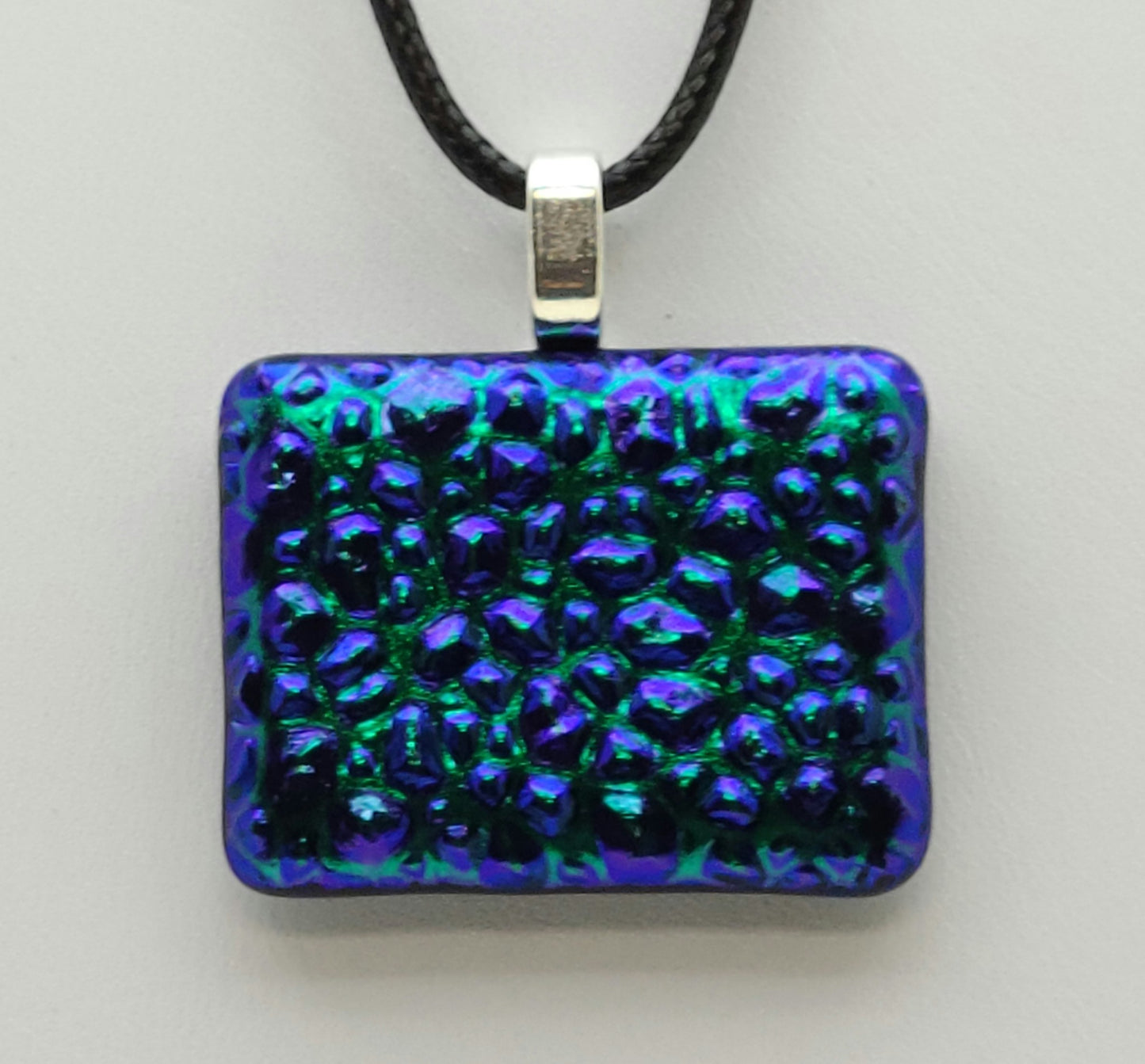 This textured dichroic fused glass pendant is purple, teal, & green.