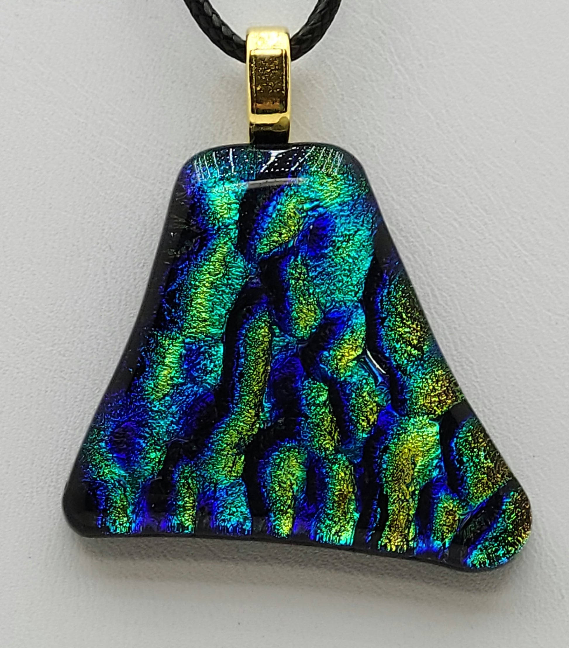 This dichroic fused glass pendant features teal, gold, & turquoise ripples.