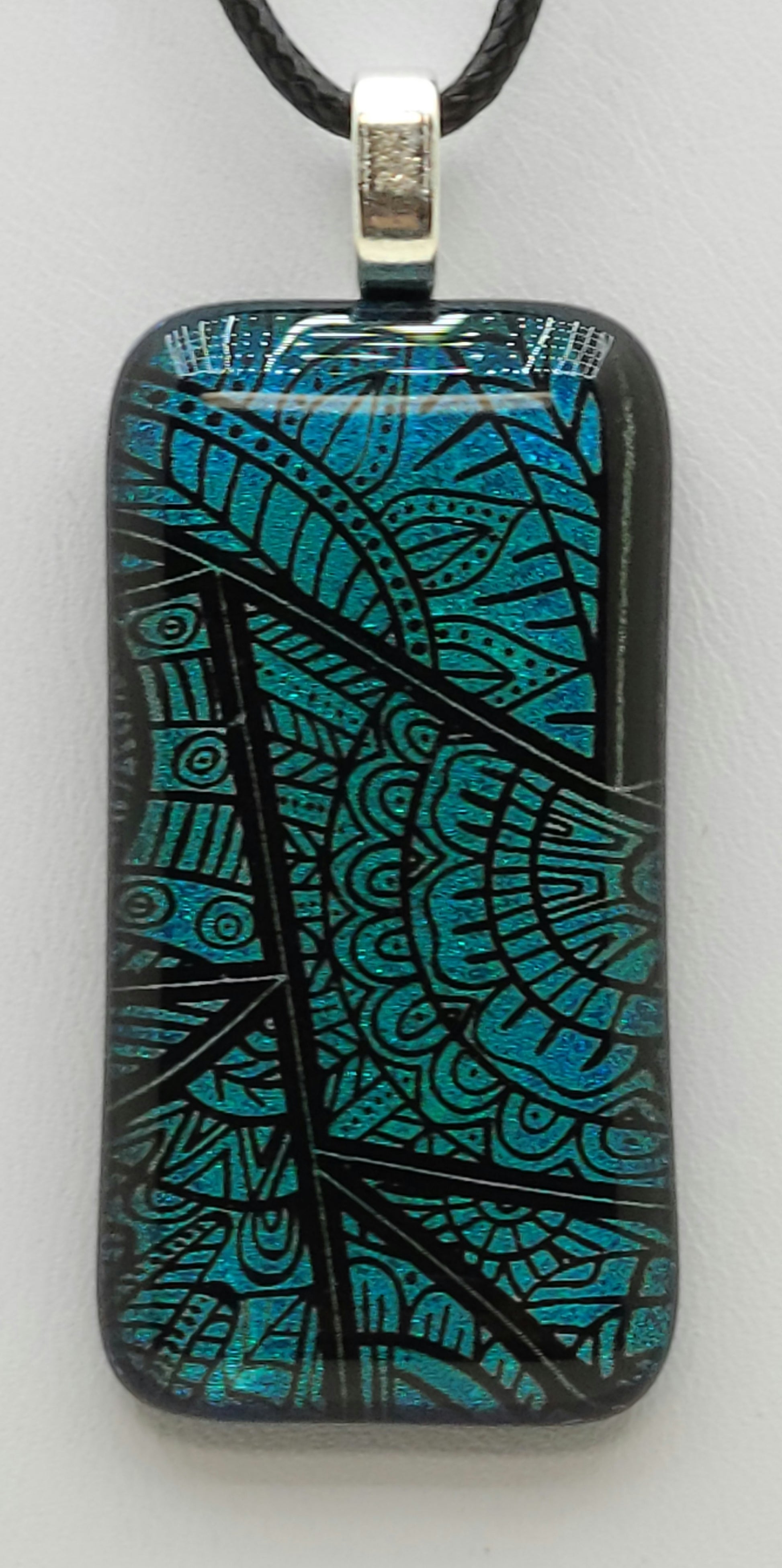 This clear capped dichroic fused glass pendant showcases stained glass window designs in teal.