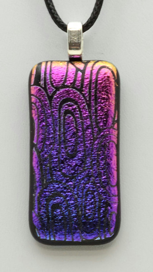 pink fades to a bluish purple in this slender dichroic fused glass pendant of etched concentric ovals.