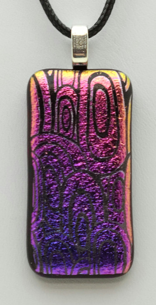 pink fades to a bluish purple in this slender dichroic fused glass pendant of etched concentric ovals.