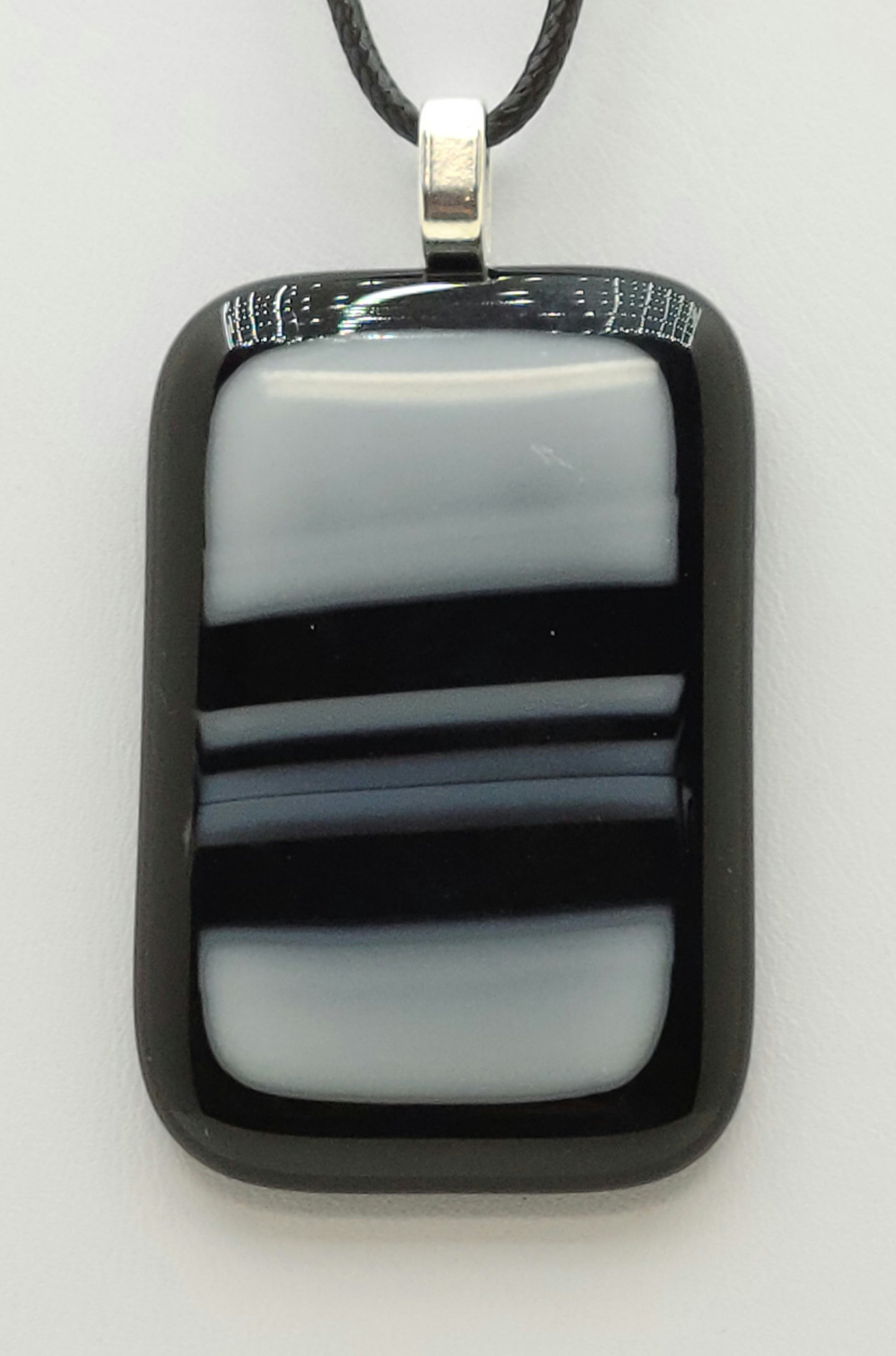 bold black strokes across white on an black background define this fused glass pendant.