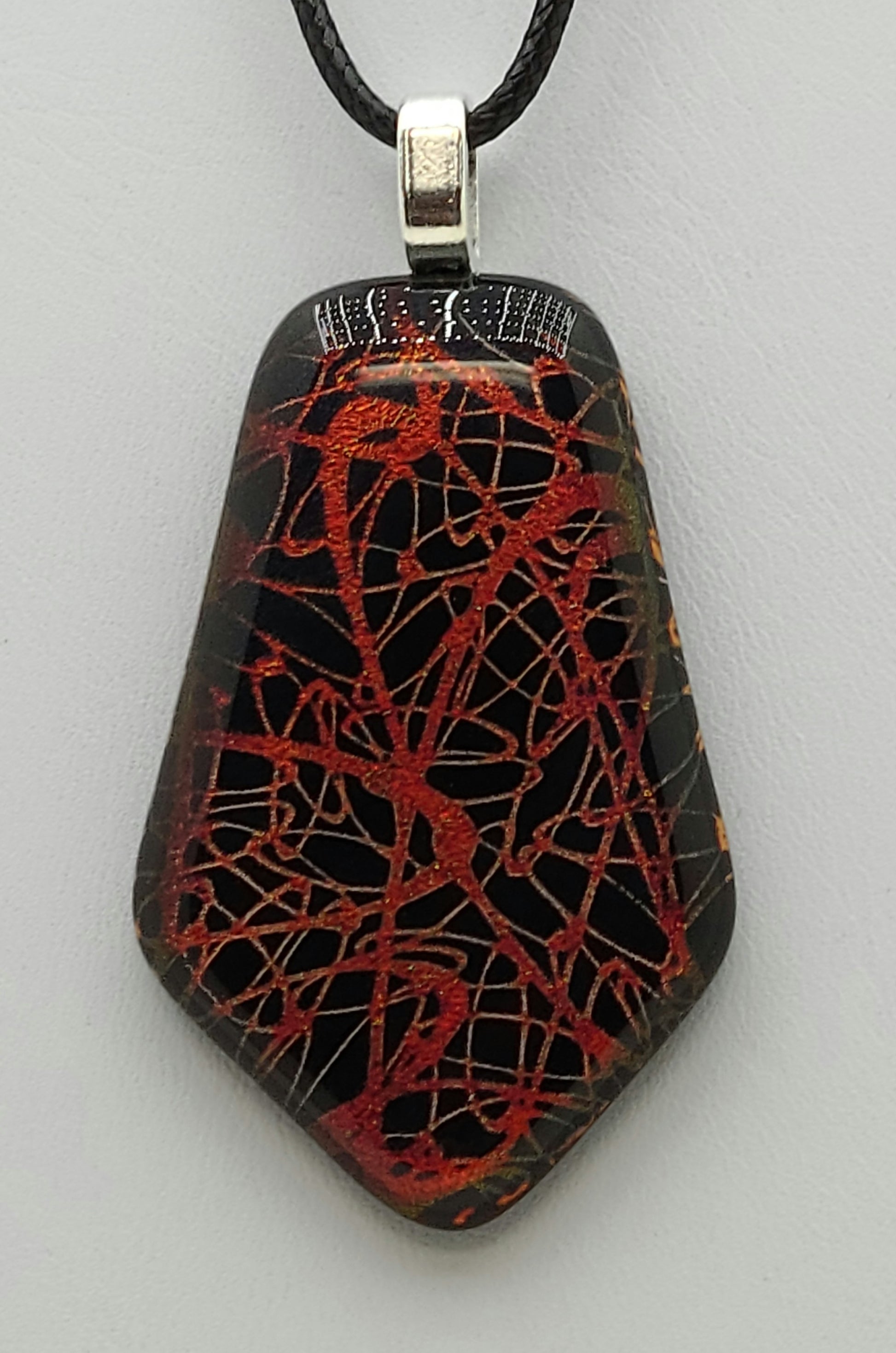 Red ovals randomly range across a black background in this dichroic fused glass pendant.