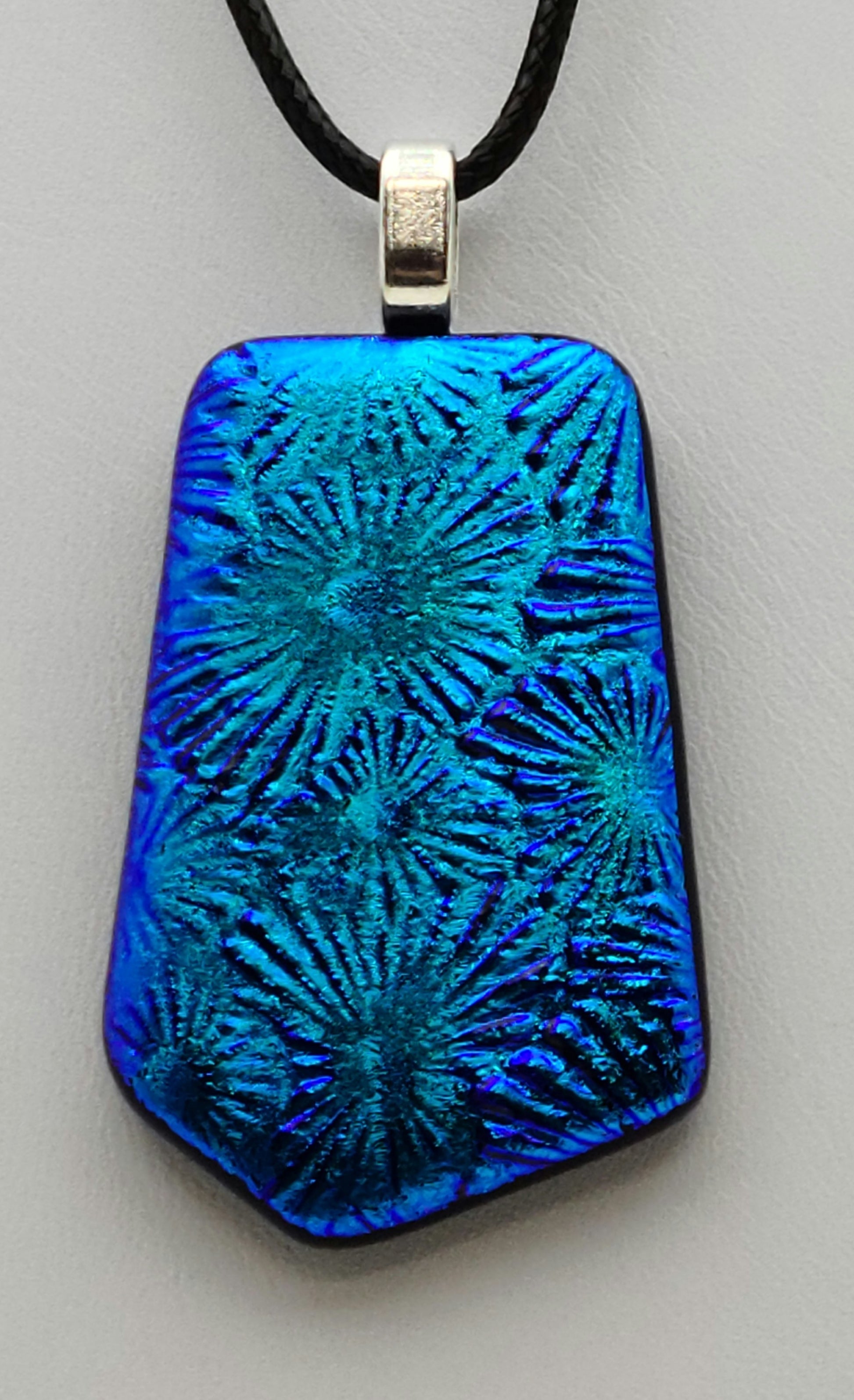 Starburst designs sing in the brilliant, deep teal blue dichroic fused glass pendant.