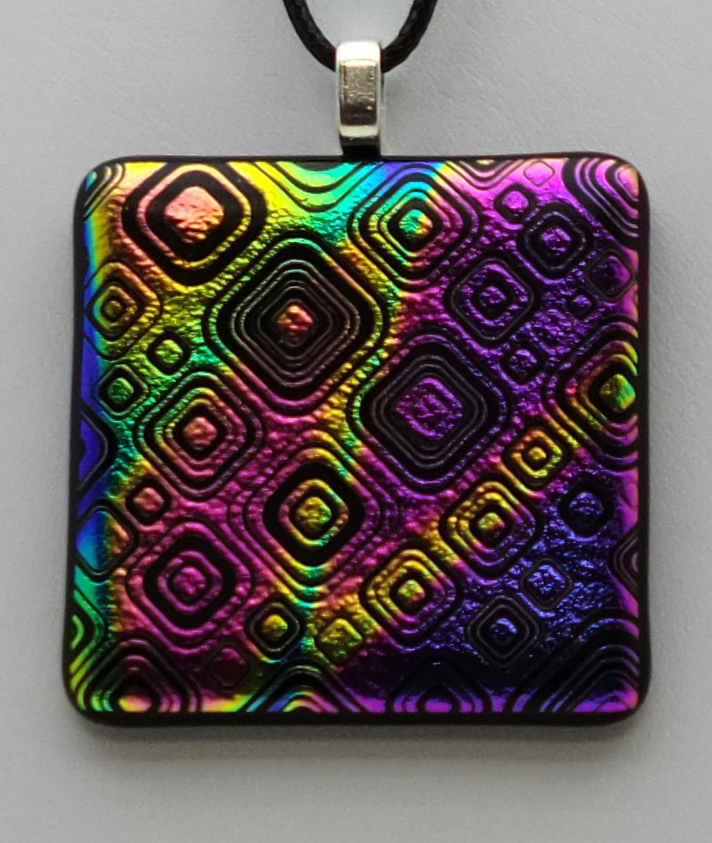 Rainbow dichroic glass has  been etched with boxes in boxes in boxes in the fused glass pendant.