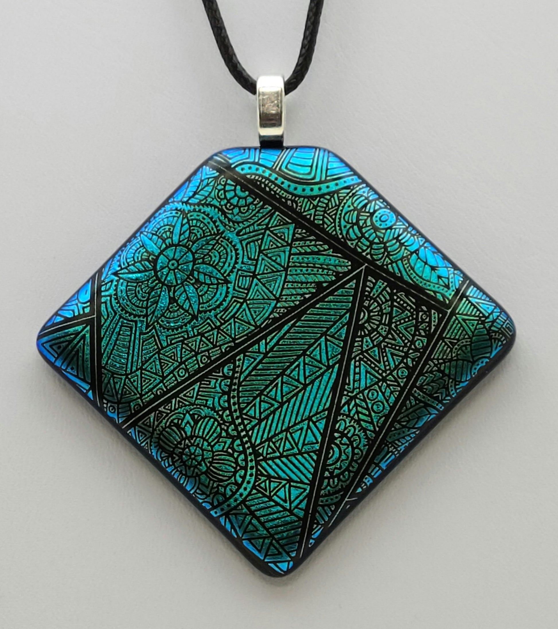 Beautiful teal dichroic glass has been etched with lovely geometric patterns in the fused glass pendant.