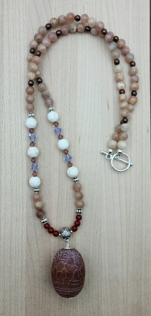 This striking Fire Agate necklace features a large, captivating fire agate pendant in rich red earth tones accented with subtle hints of peach and lavender.