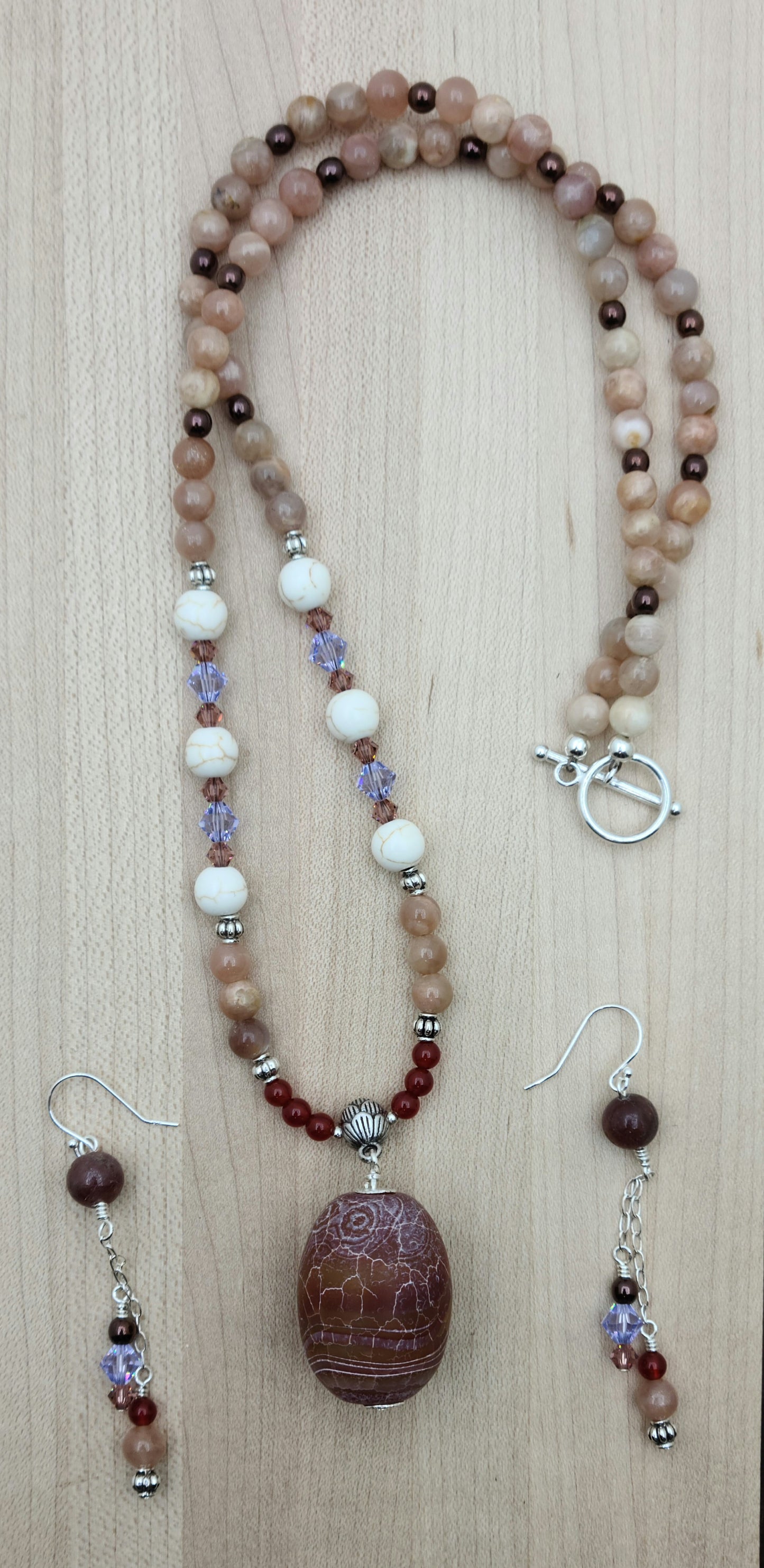 This striking Fire Agate necklace and earrings set features a large, captivating fire agate pendant in rich red earth tones accented with subtle hints of peach and lavender.