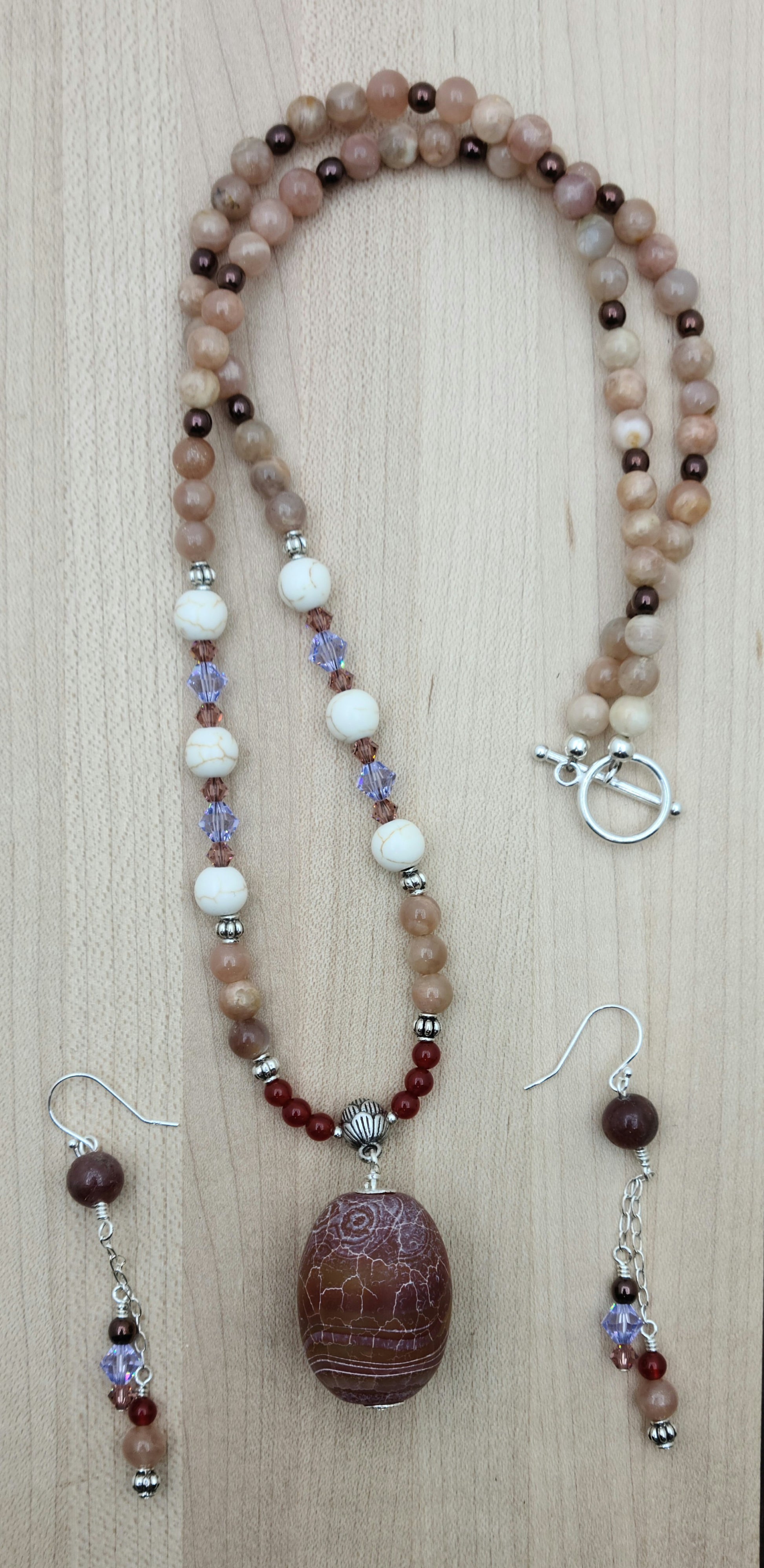 This striking Fire Agate necklace and earrings set features a large, captivating fire agate pendant in rich red earth tones accented with subtle hints of peach and lavender.