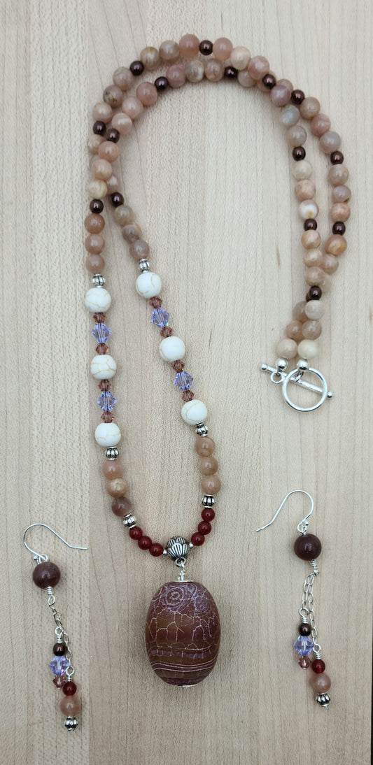 This striking Fire Agate necklace and earrings set features a large, captivating fire agate pendant in rich red earth tones accented with subtle hints of peach and lavender.