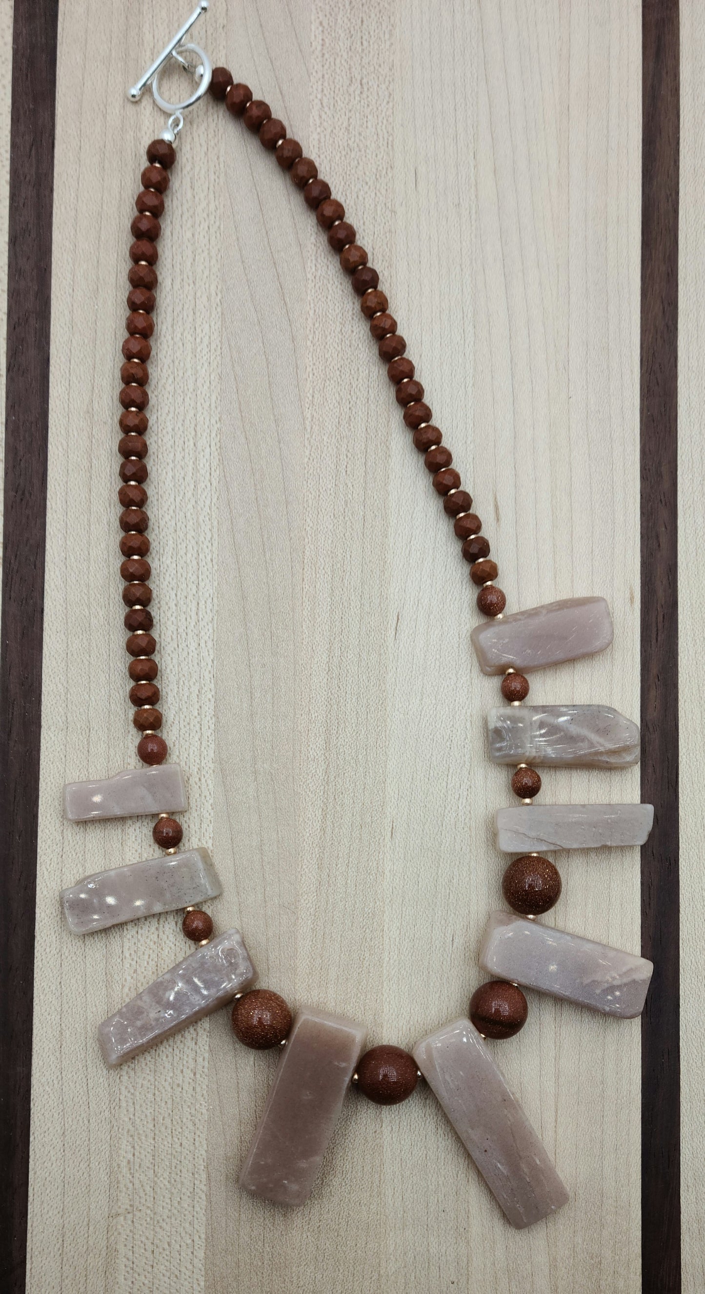 This Moonstone Slab Necklace features striking free-form peach moonstone slabs, enhanced by the sparkling contrast of goldstone and the warm tones of chocolate howlite rondelles.