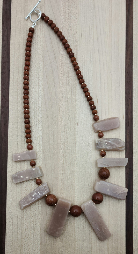 This Moonstone Slab Necklace features striking free-form peach moonstone slabs, enhanced by the sparkling contrast of goldstone and the warm tones of chocolate howlite rondelles.