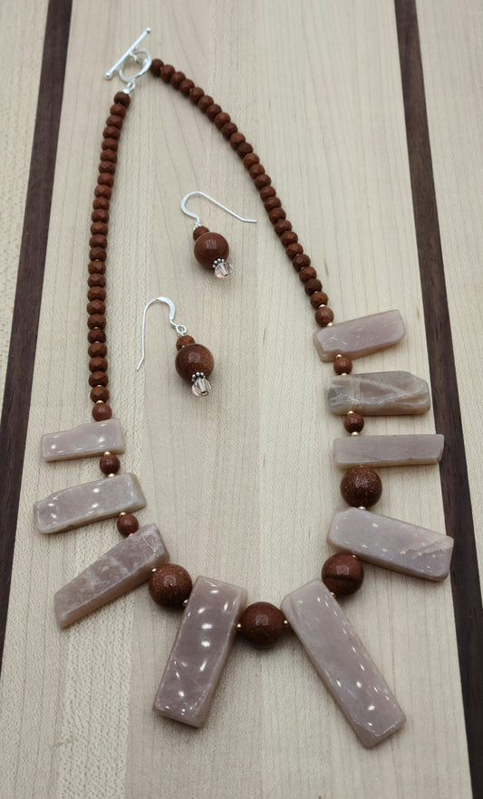This Moonstone Slab Necklace & Earrings set features striking free-form peach moonstone slabs, enhanced by the sparkling contrast of goldstone and the warm tones of chocolate howlite rondelles.