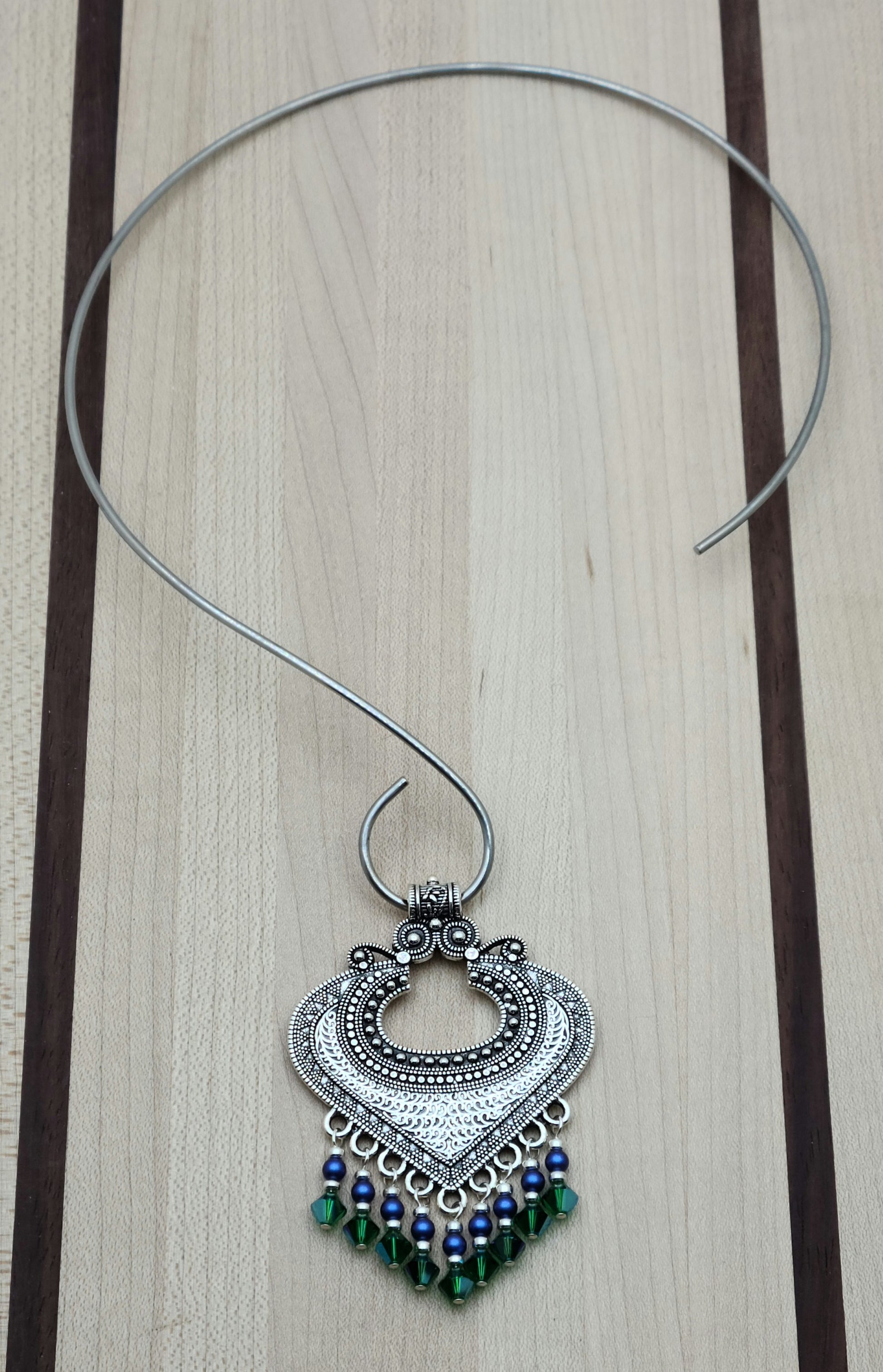 large pewter bali style pendant with bright blue and rich green dangles hanging on a stainless steel neck wire