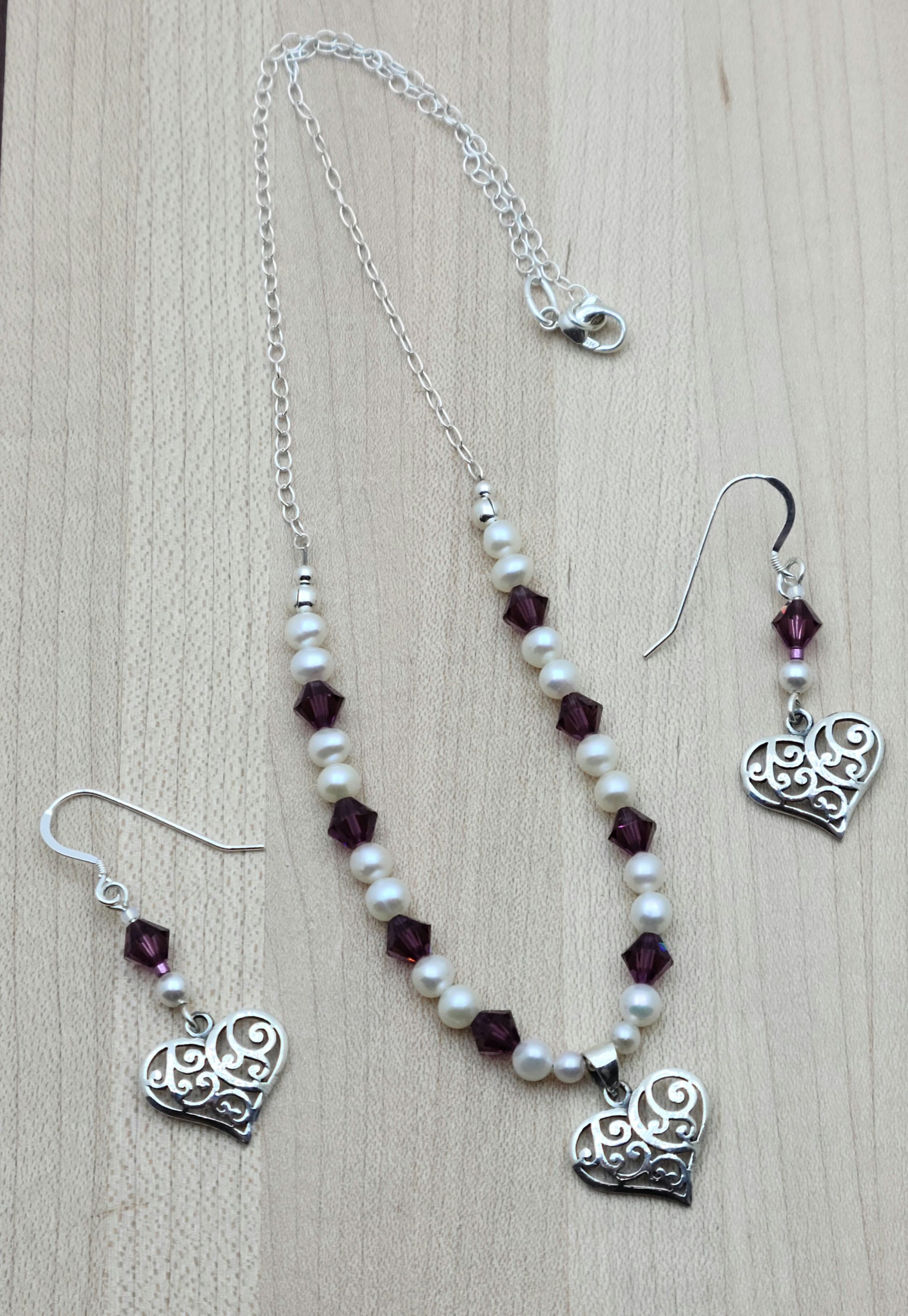 This sophisticated & sweet set features luminous white freshwater pearls & vibrant amethyst crystals, accented by a delicate filigree sterling silver heart pendant with matching earrings