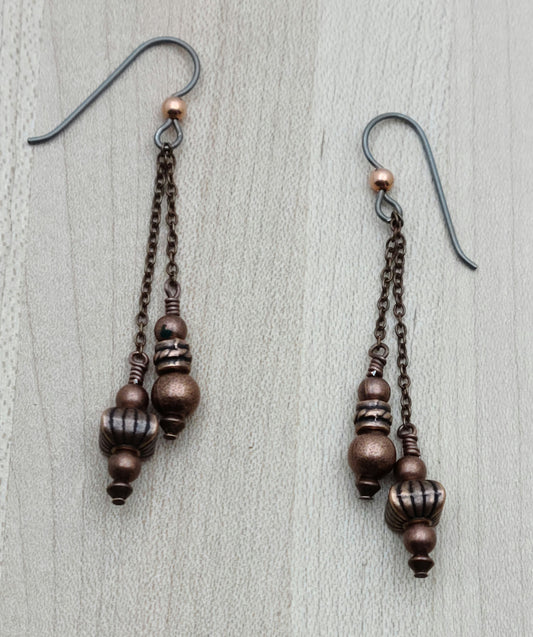Brighten your day with these Antique Copper Dangle Earrings, featuring a charming array of unique antique copper beads that catch every eye. Playfully suspended from antique copper wire and secured with hypoallergenic niobium French hook ear wires, they blend vintage flair with comfort for sensitive ears. Perfect for adding a touch of whimsy to any outfit!