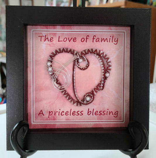 Shadow box with burgundy & silver woven wire heart. Background print of weathered fabric is printed on canvas medium and reads "The Love of family is a priceless blessing."