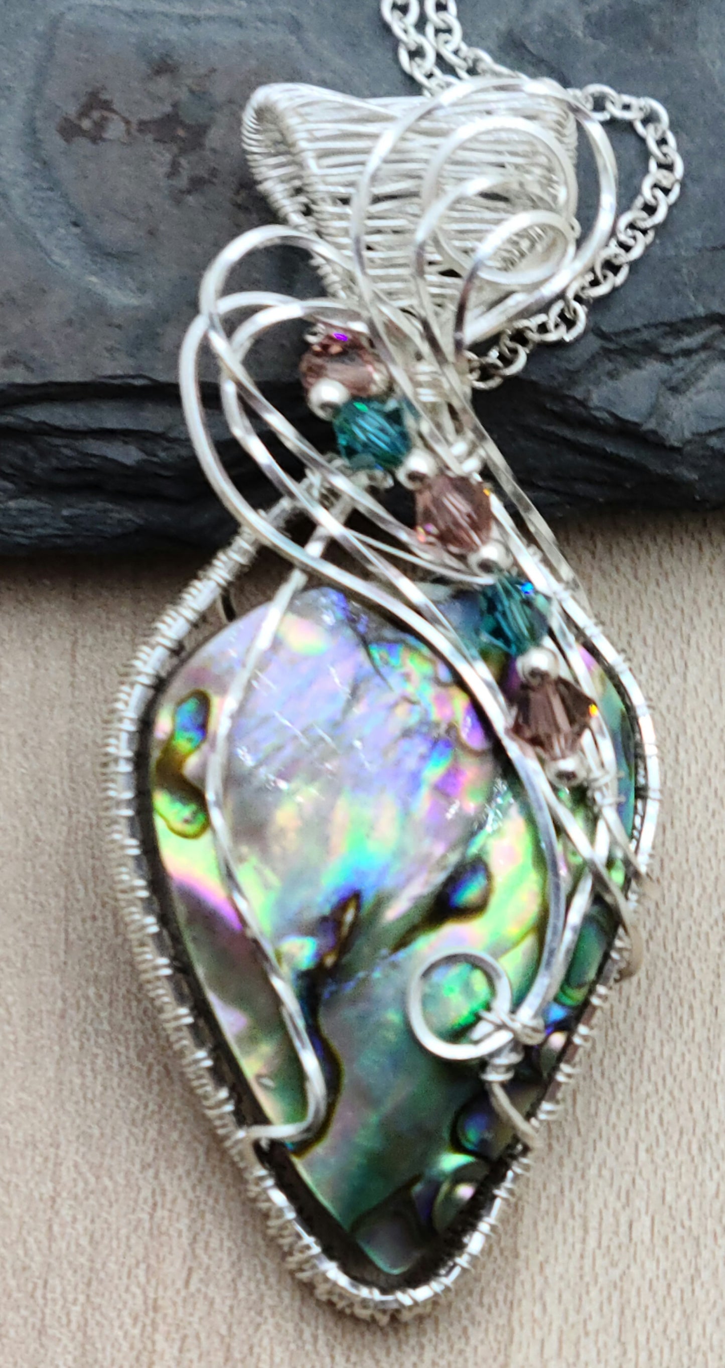 Prepare to be mesmerized by this radiant iridescent abalone shell pendant in a woven silver filled wire frame!
